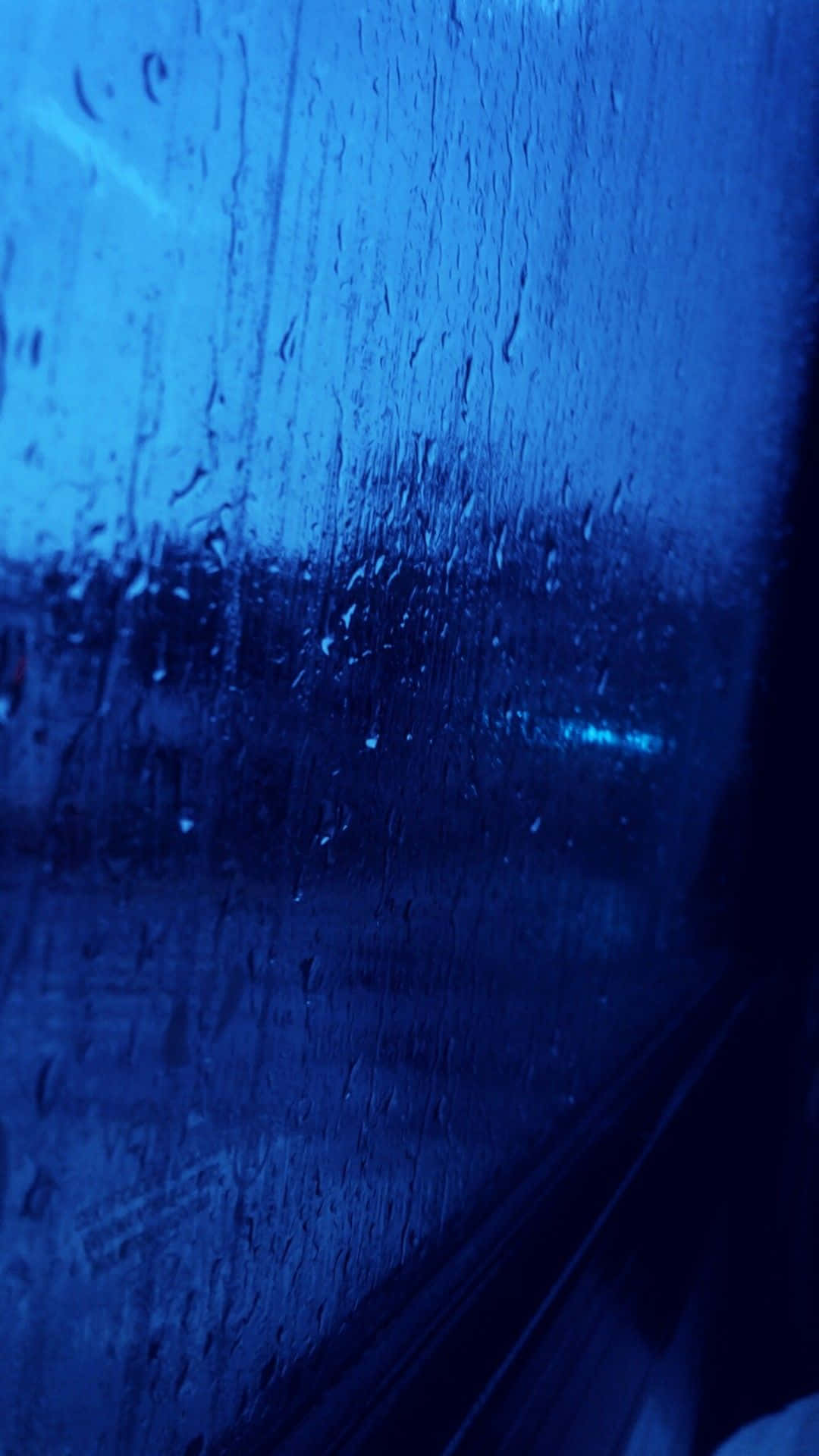 深藍色美學動圖 桌布 壁紙 — 雨滴沿著車窗流下，在深藍色夜燈下，顯露出模糊的城市燈光。