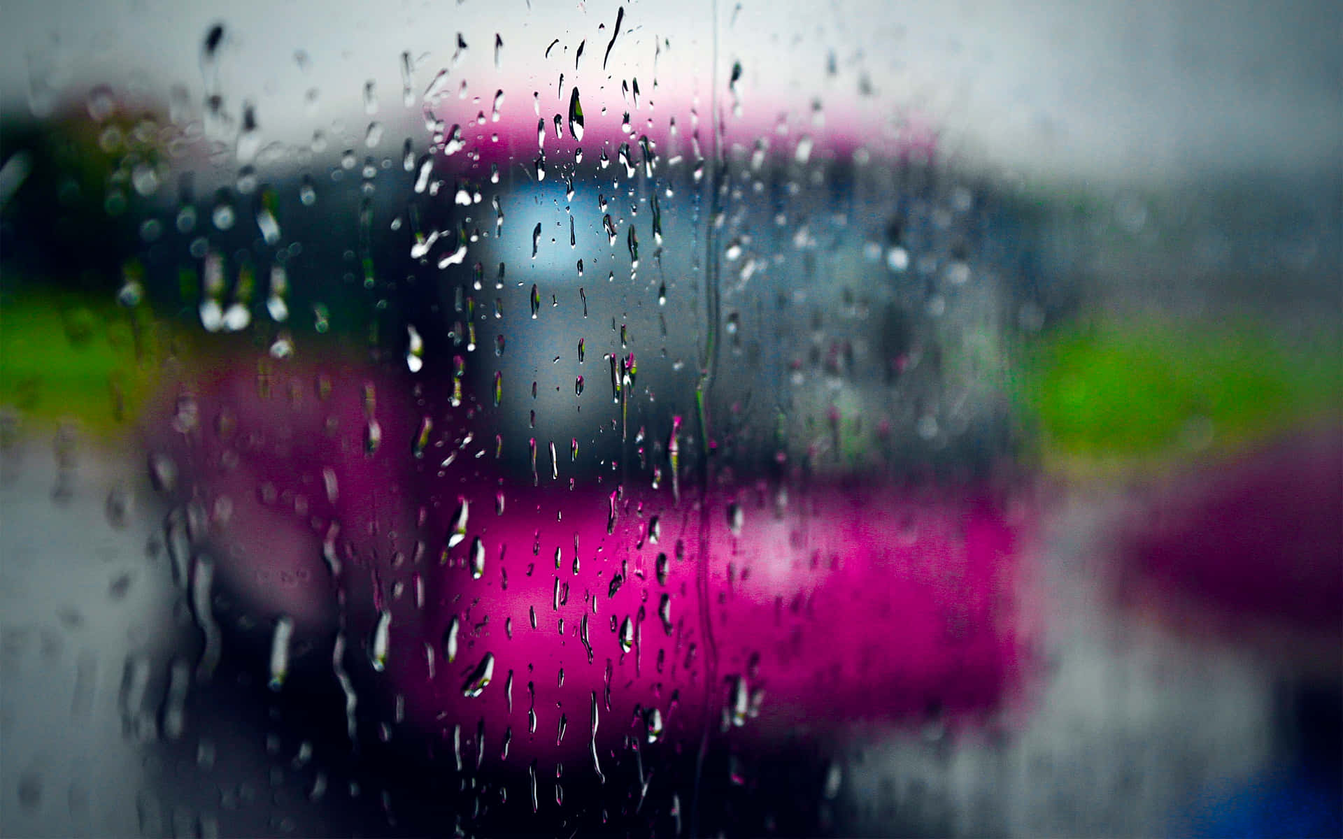 Rain Desktop 桌布 壁紙 — 雨滴沿著車窗流下，將充滿活力的粉紅色和綠色城市燈光模糊成夢幻般的散景光暈。