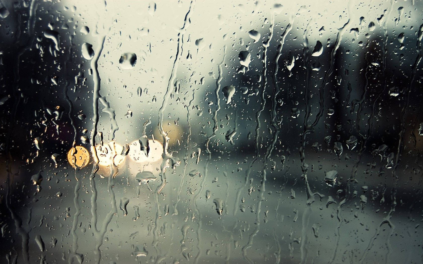 Rainy Day 桌布 壁紙 — 雨滴沿著車窗流下，將溫暖的路燈模糊成發光球體，映襯著灰色的城市背景。