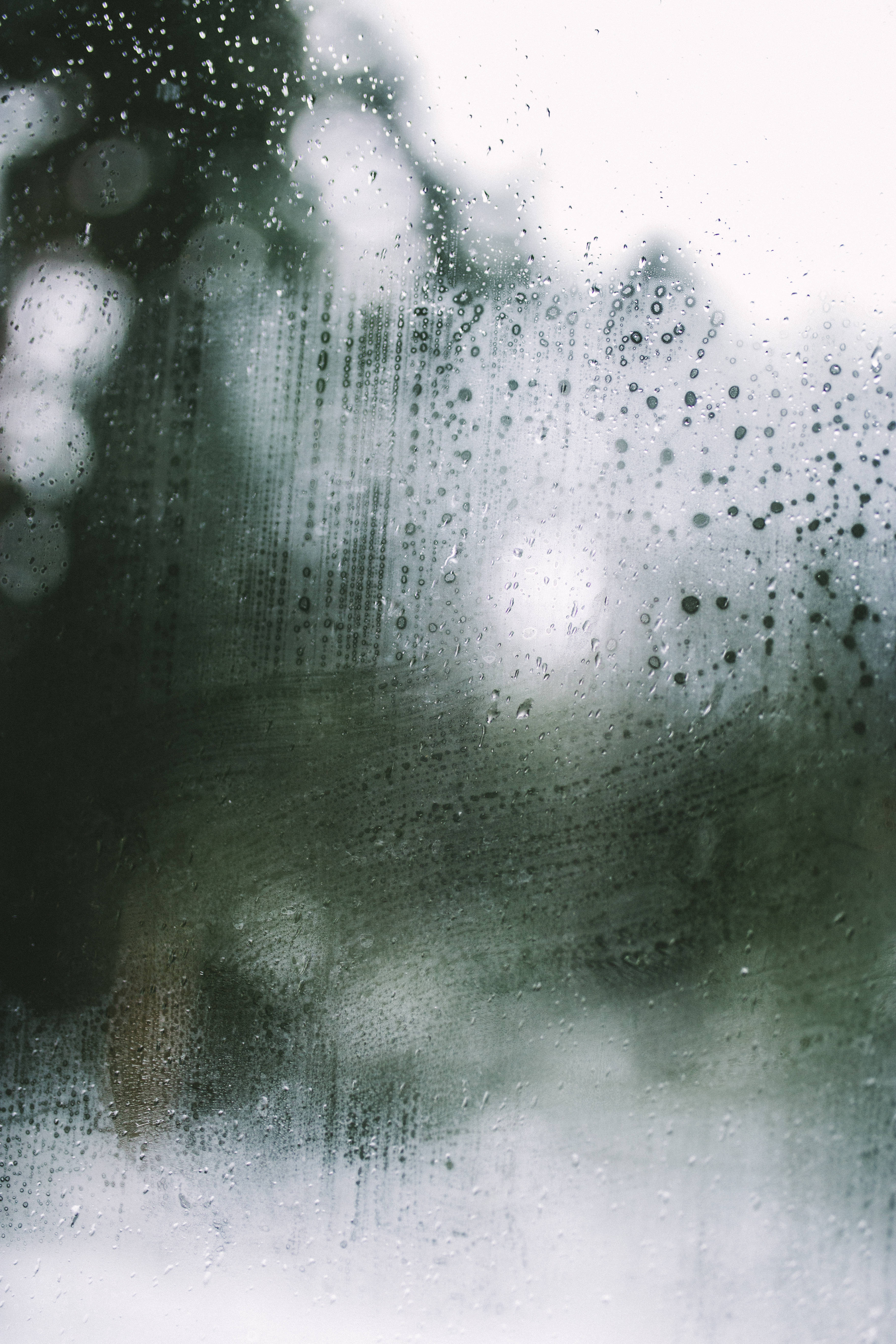 make it rain 桌布 壁紙 — 雨滴沿著霧氣朦朧的窗戶流下，顯露出模糊的綠色樹葉和柔和的白色光線。