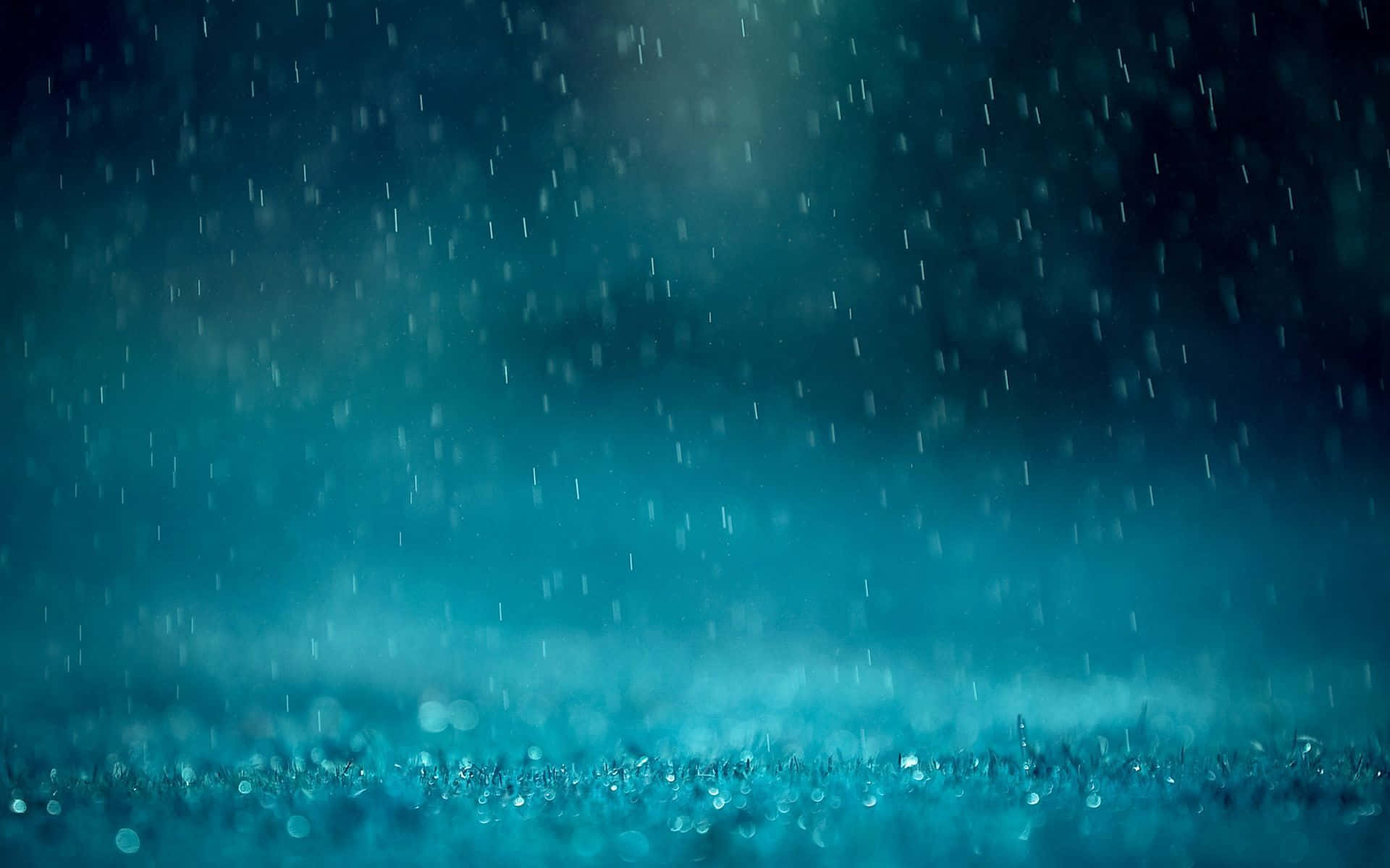 Raining 桌布 壁紙 — 雨滴落在深藍綠色背景上，前景草地有發光的散景燈光。
