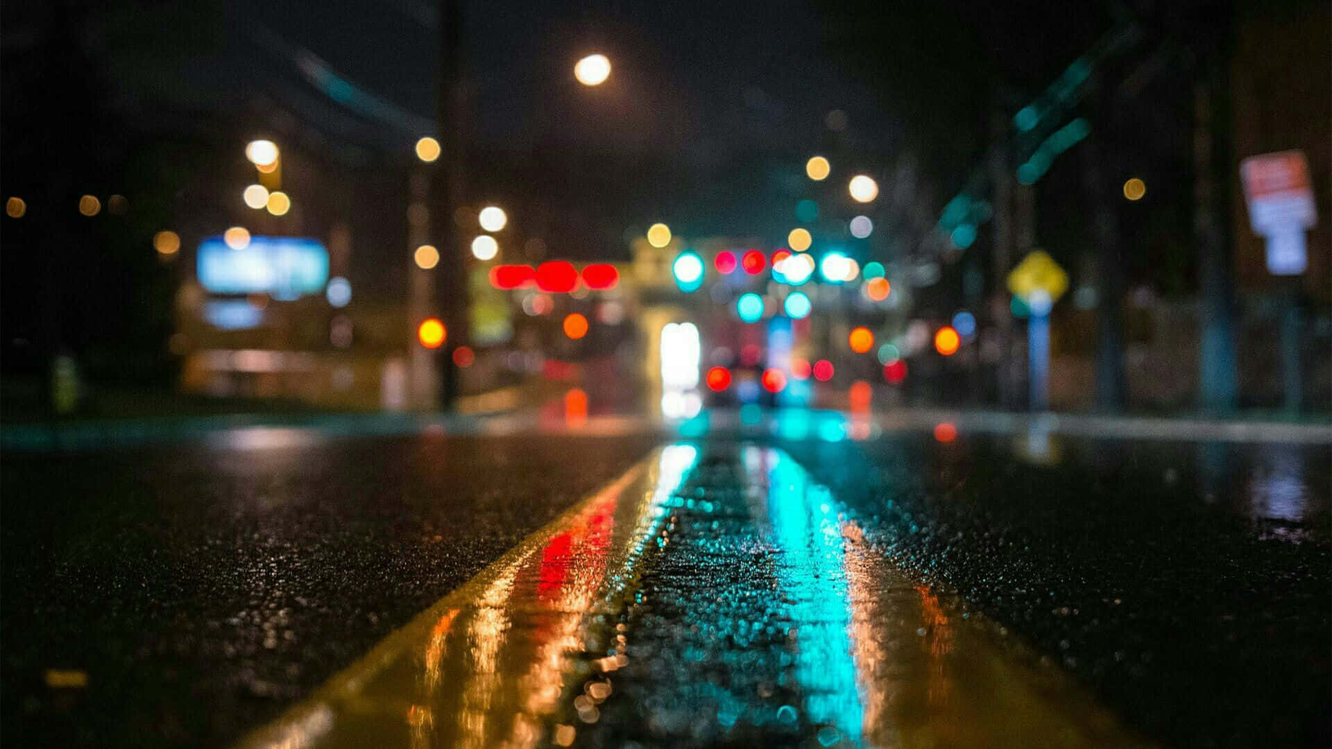 Rainy 桌布 壁紙 — 雨濕的城市街道夜晚，發光的散景燈光反射在濕瀝青和黃色中心線上。
