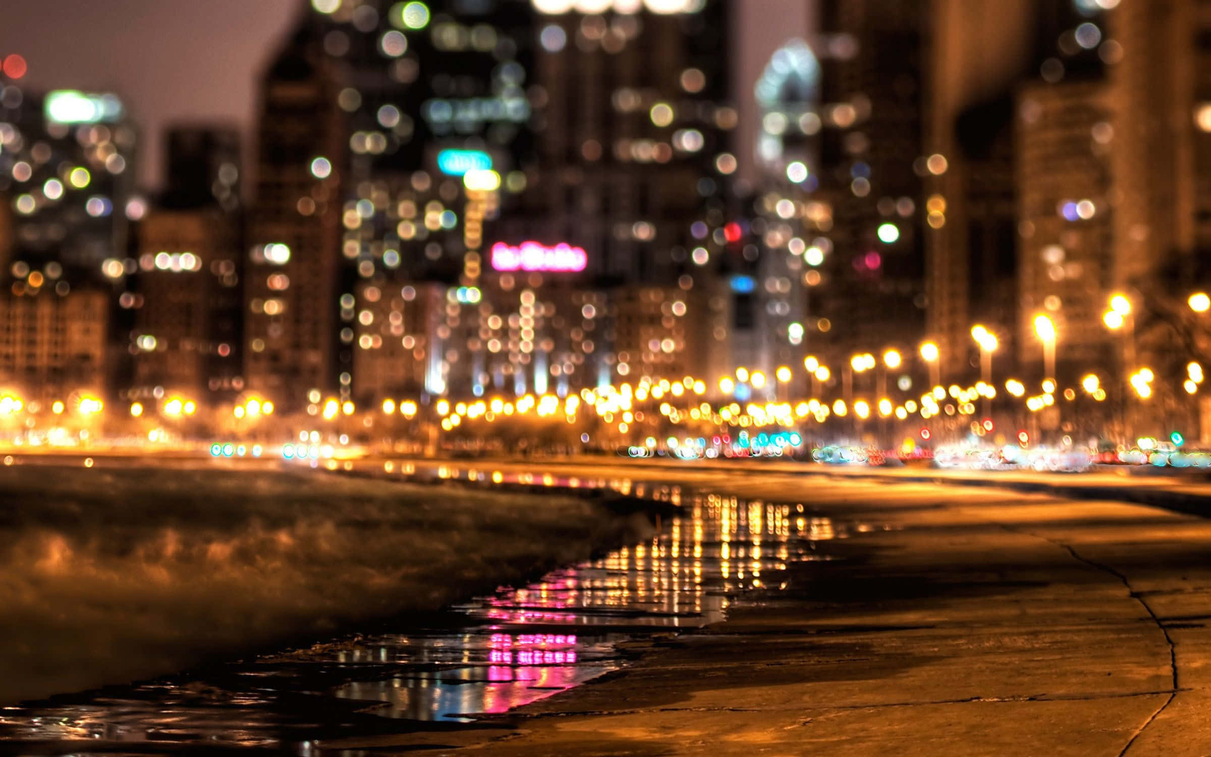 City Street 桌布 壁紙 — 雨濕的夜晚城市人行道反射著高聳摩天大樓和路燈的模糊散景燈光。