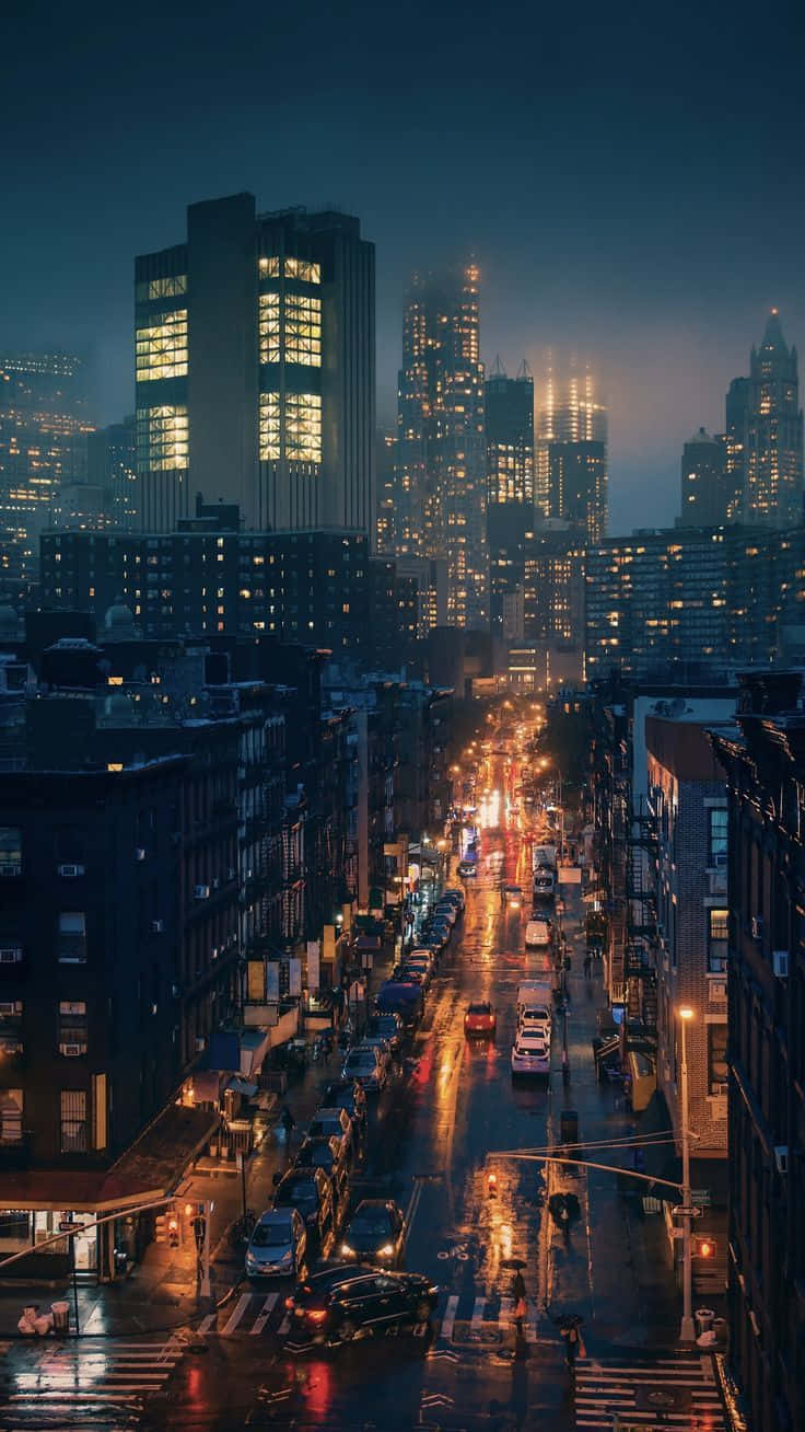 夜空 桌布 壁紙 — 雨濕的夜晚城市街道，在深藍色天空下反射著發光的街燈和建築物窗戶。