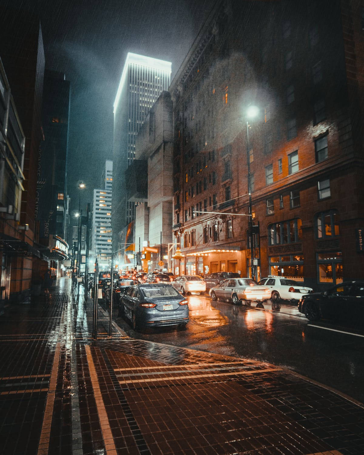 夜景城市 桌布 壁紙 — 雨濕的夜晚城市街道，發光的車頭燈在高聳建築物之間的濕漉漉路面上反射。