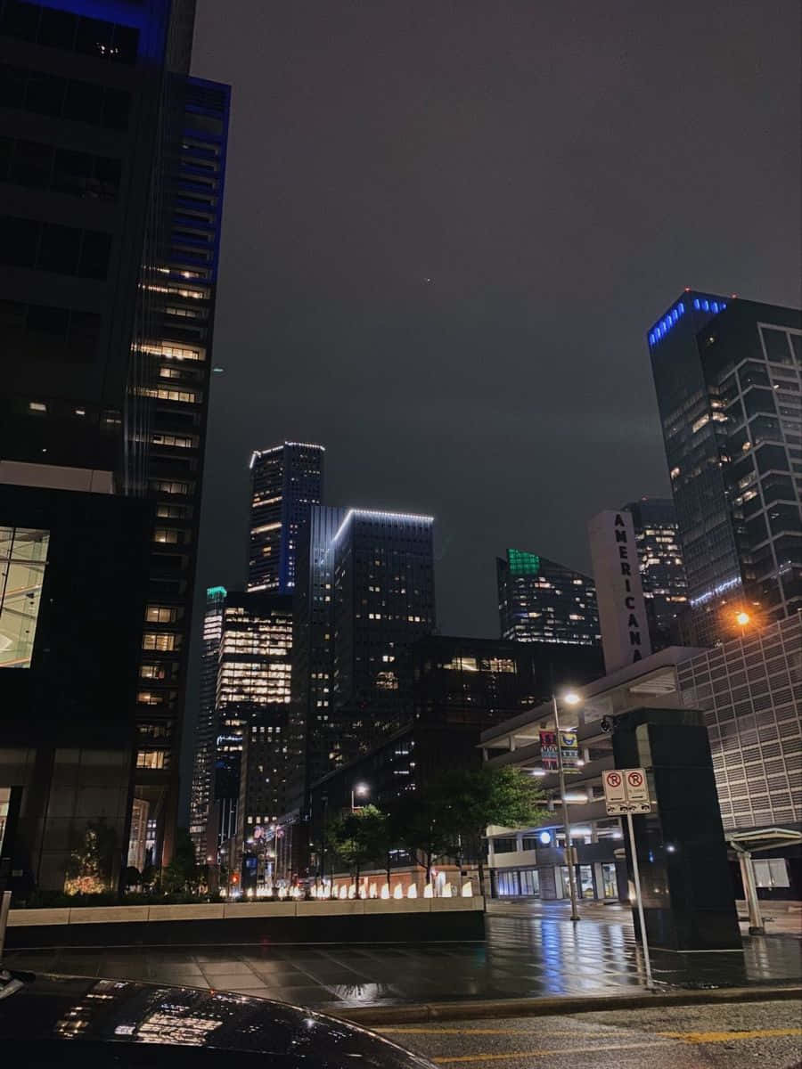 dallas 桌布 壁紙 — 雨濕的夜晚城市街道，高聳的摩天大樓在黑暗的天空下閃耀。