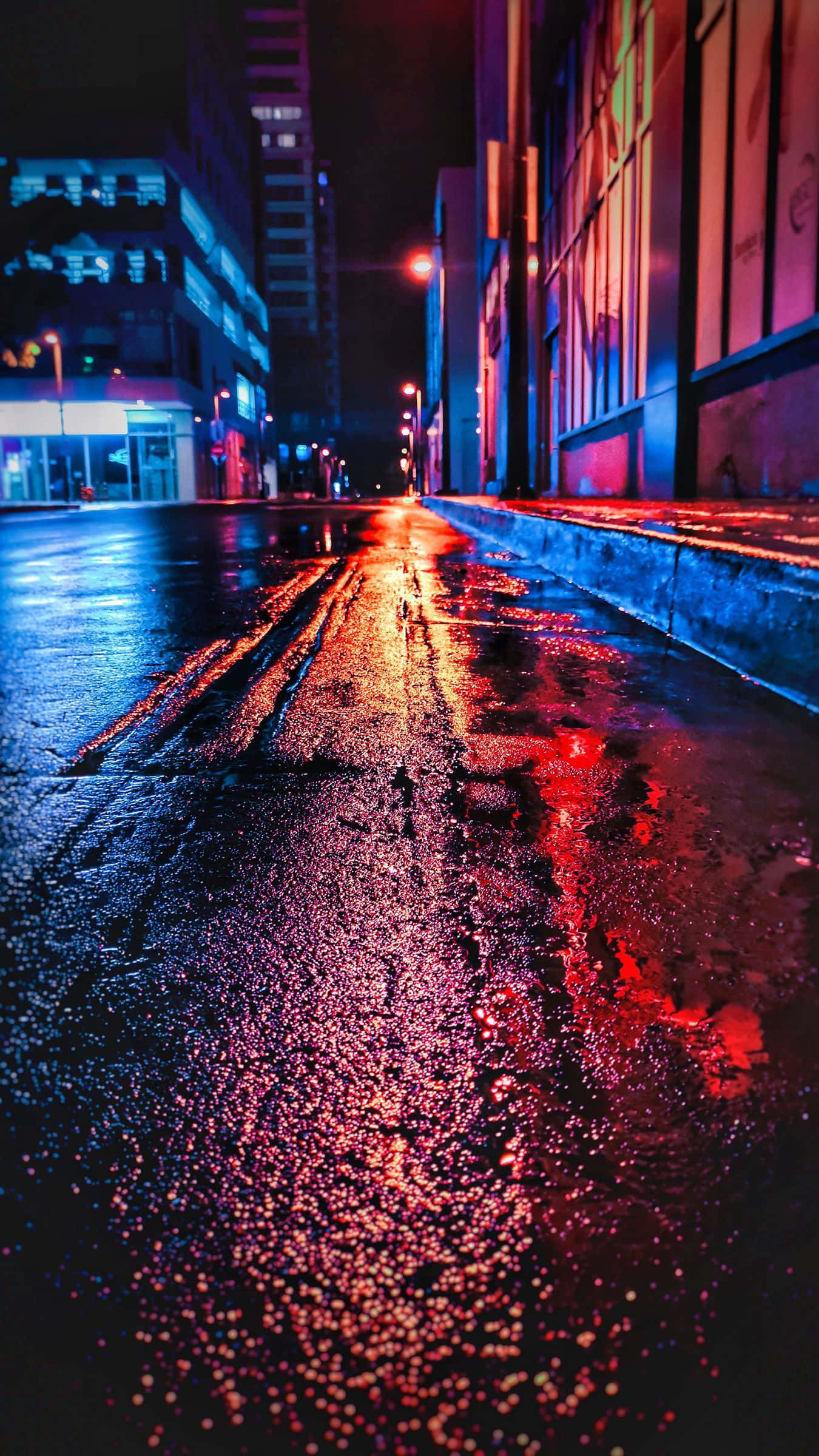 iPhone Neon 桌布 壁紙 — 雨濕的夜晚城市街道在街燈下反射出鮮豔的紅色和藍色霓虹燈光。
