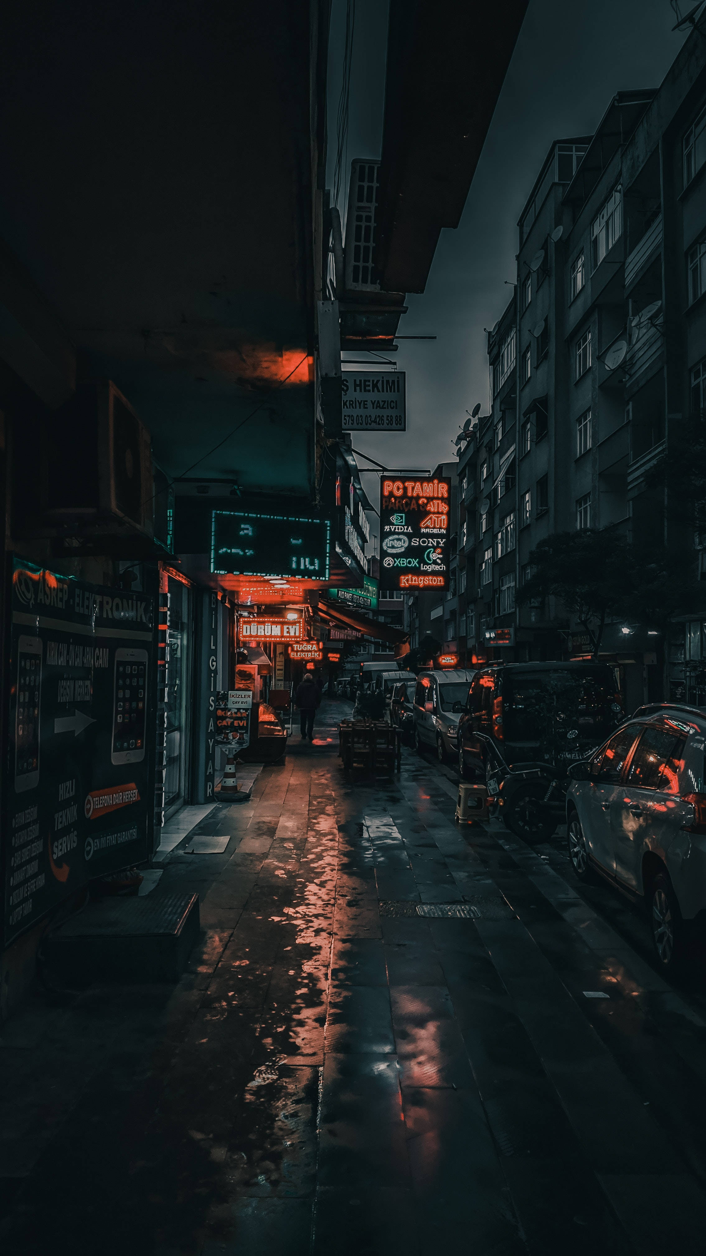 neon sign 桌布 壁紙 — 雨濕的夜間城市小巷，霓虹招牌在停泊的汽車和高樓大廈之間的濕漉漉路面上反射發光。