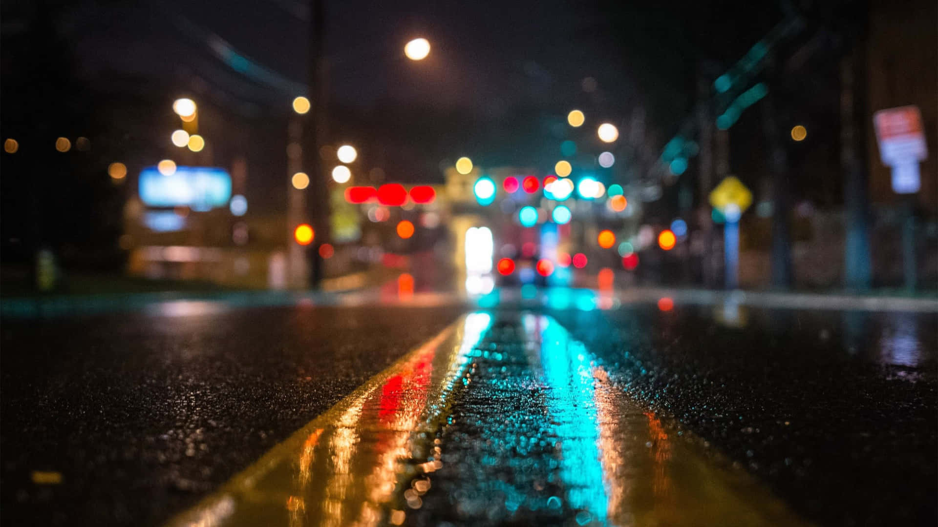 4K 桌布 桌布 壁紙 — 雨濕的夜間城市街道，濕漉漉的瀝青和黃色車道標記上反射著發光的散景燈光。