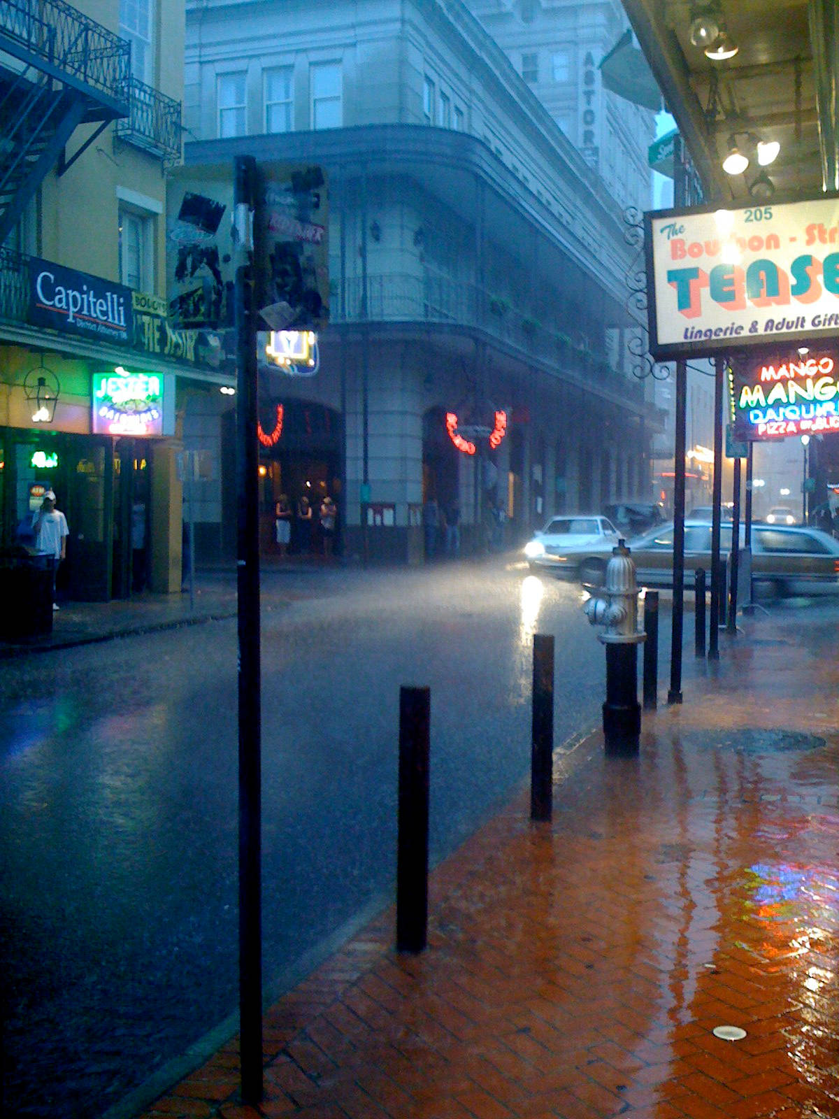 Raining 桌布 壁紙 — 雨濕的夜間城市街道，發光的霓虹燈招牌映照在潮濕的路面和磚砌人行道上。