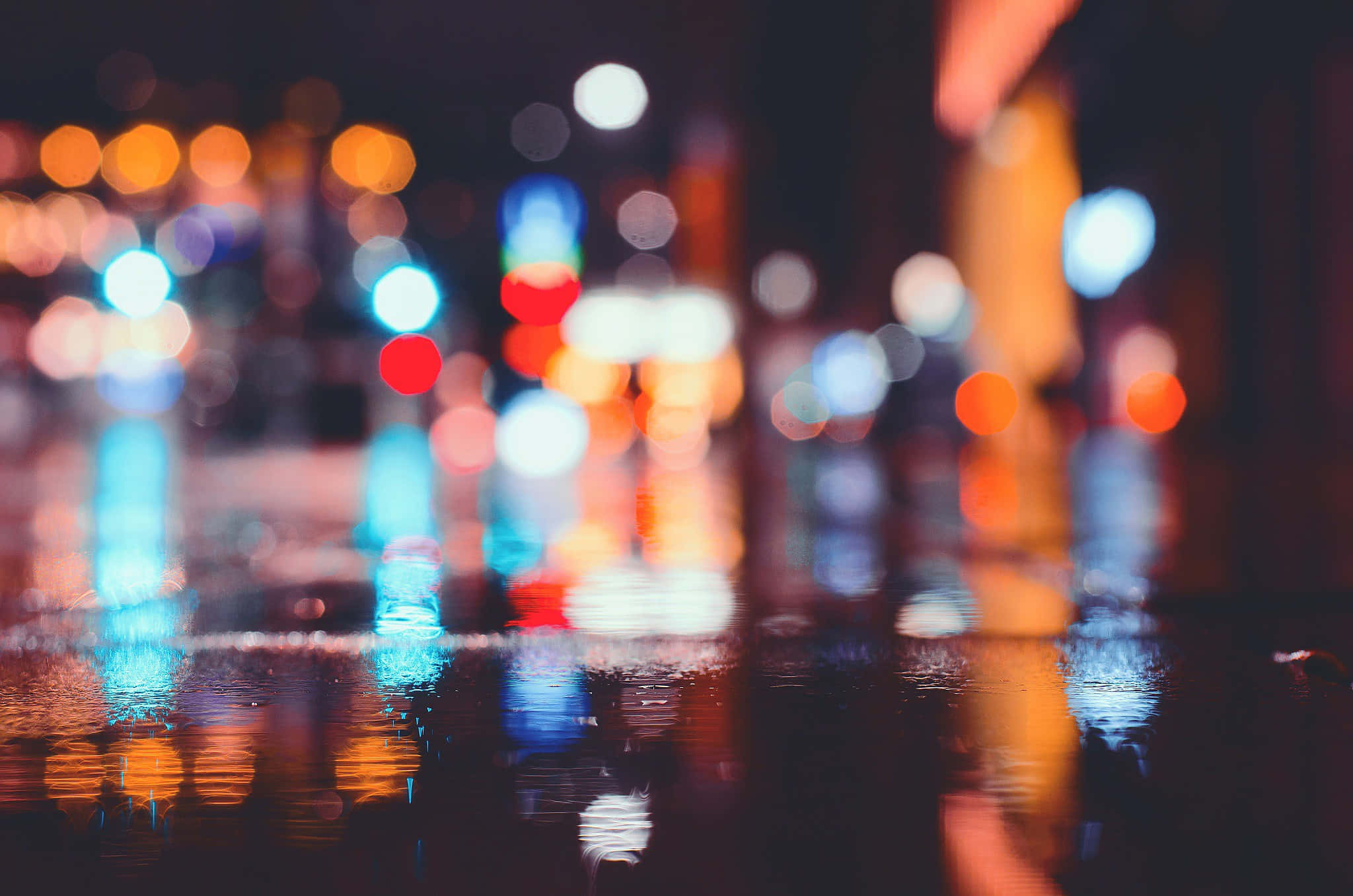 City At Night 桌布 壁紙 — 雨濕的夜間城市街道，鮮豔的散景燈光在水坑中反射，營造出夢幻般的發光效果。