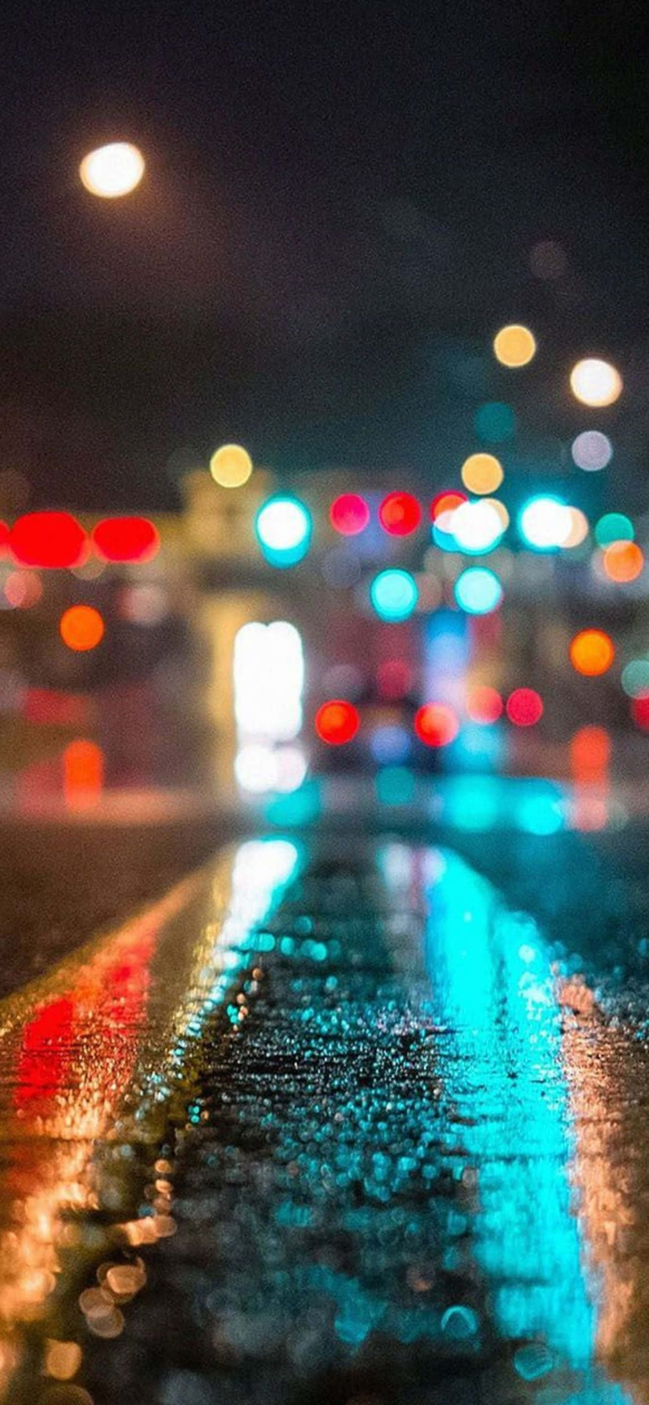 酷炫iPhone 桌布 壁紙 — 雨濕的夜間城市街道反射來自交通和街燈的發光散景燈光。