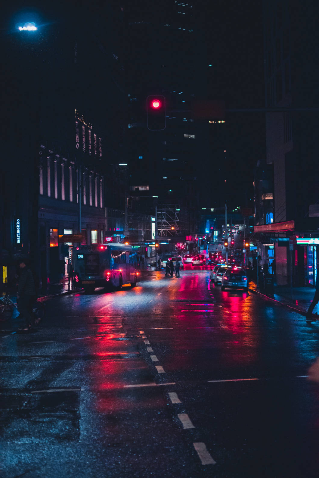 iPhone 桌布 壁紙 — 雨濕的夜間城市街道在紅色交通號誌下反射來自汽車和建築物的霓虹燈光。