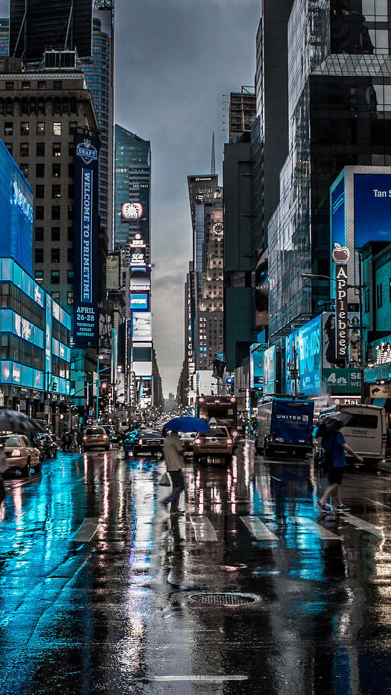 New York City Night iPhone 桌布 壁紙 — 雨濕的時代廣場在夜晚反射著霓虹燈牌和高聳的摩天大樓，行人撐著傘穿過濕漉漉的街道。