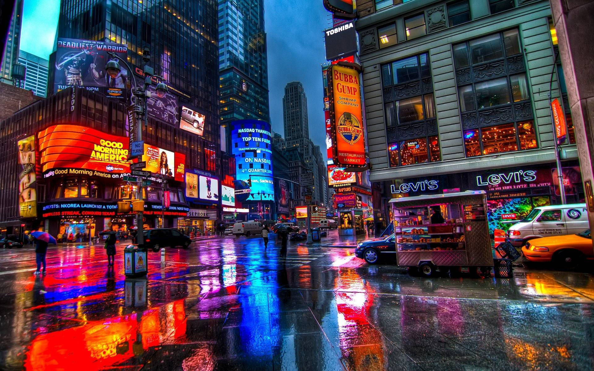 美學 桌布 壁紙 — 雨濕的時代廣場在夜晚反射霓虹燈牌和高聳的廣告看板，呈現出令人眼花撩亂的城市景觀。