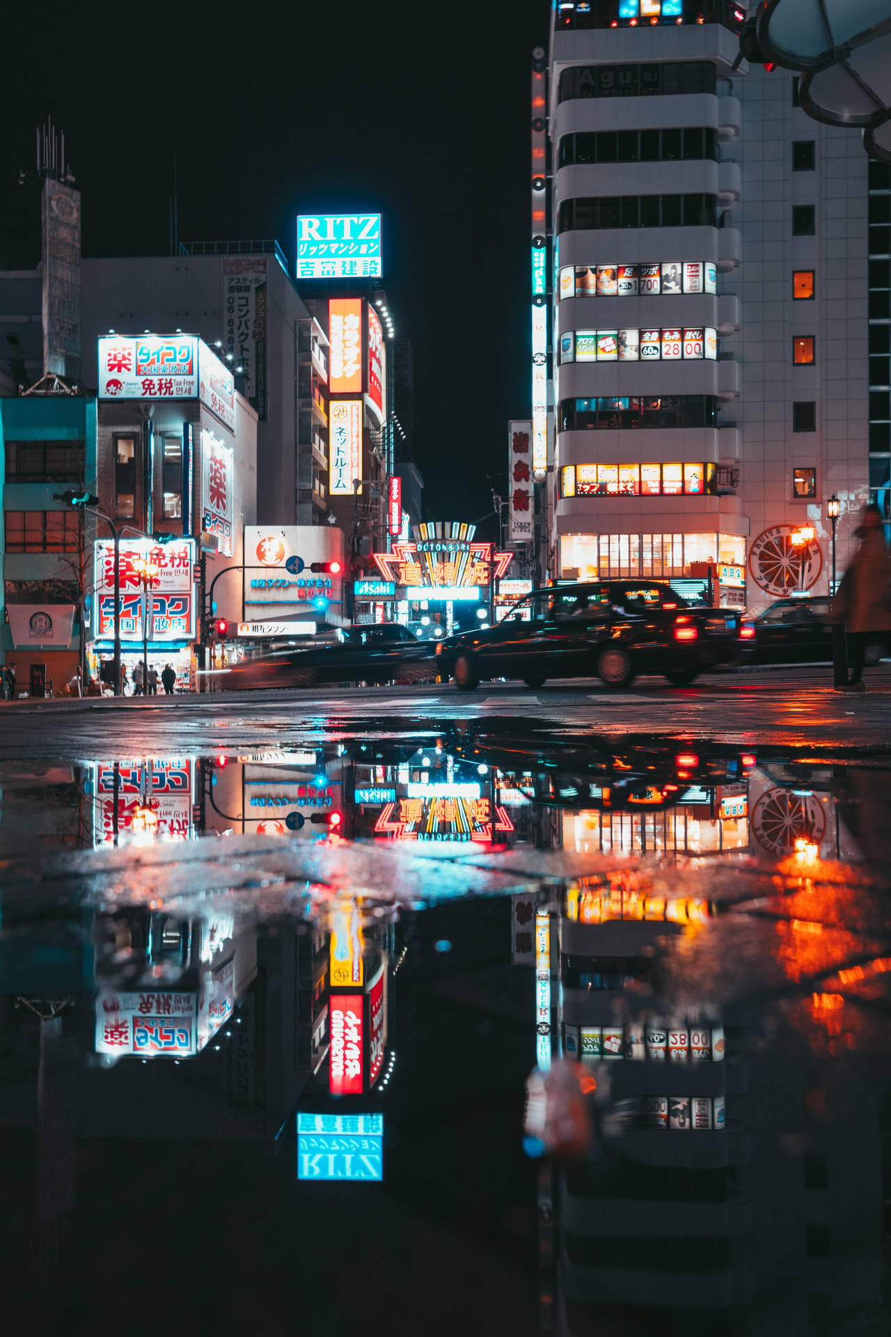 霓虹燈照亮的東京夜晚街道，在雨水坑中反射出移動的汽車。
