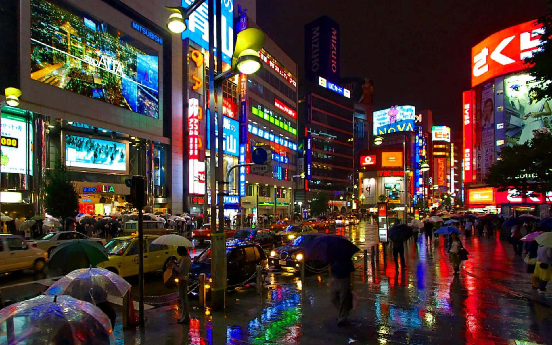 東京 桌布 壁紙 — 雨濕的東京夜晚街道，霓虹招牌在濕漉漉的人行道上閃爍反射，行人撐著雨傘。