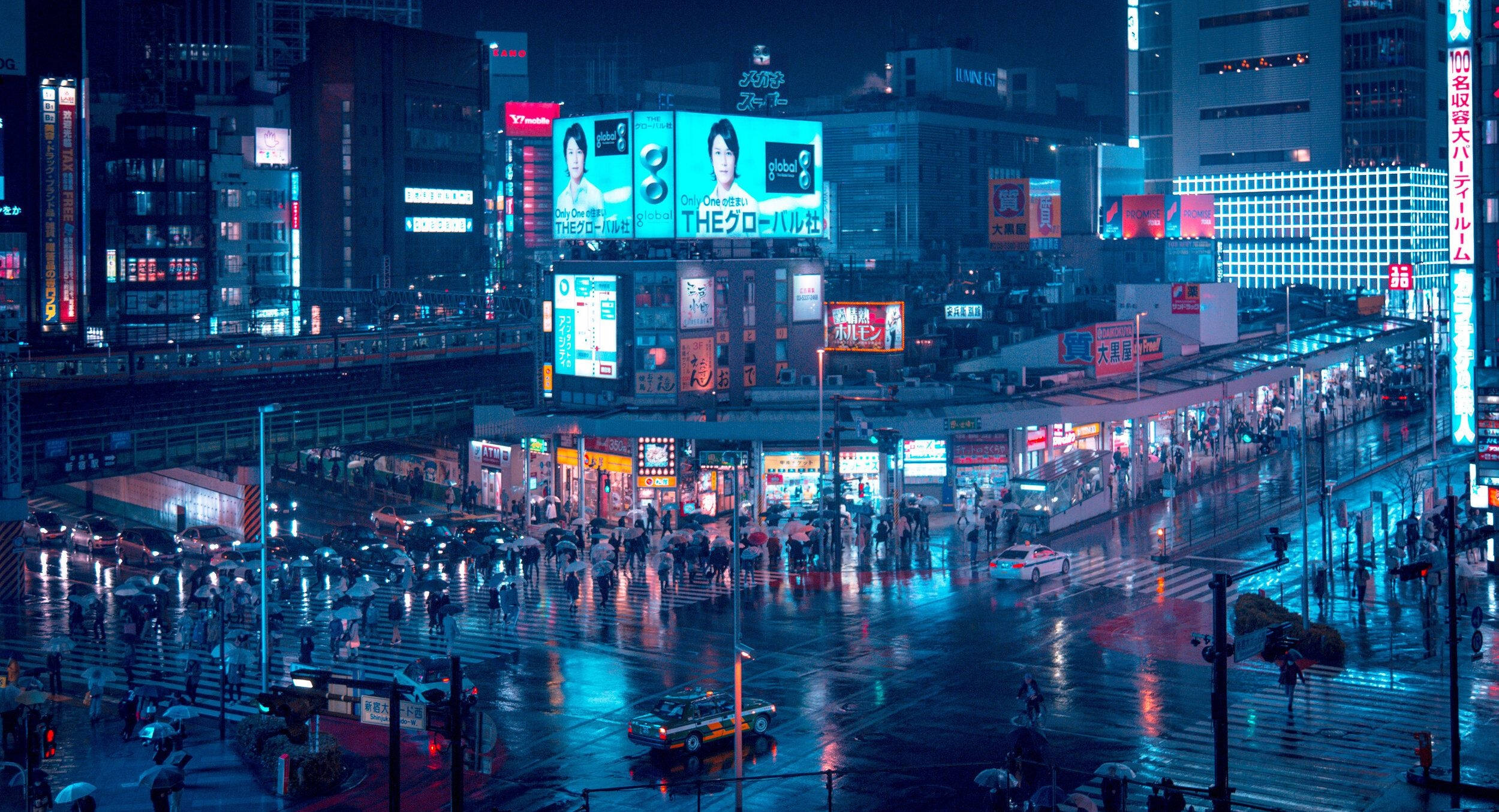 日本 桌布 壁紙 — 雨濕的東京夜晚街道，霓虹燈光在濕漉漉的路面上反射，人群在高聳的廣告牌下穿行。