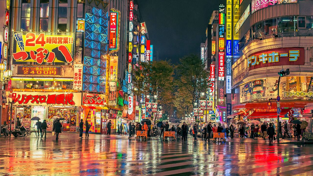 東京 桌布 壁紙 — 雨濕的東京夜晚街道反射出耀眼的霓虹燈牌和熙攘的行人，在發光的廣告牌下。