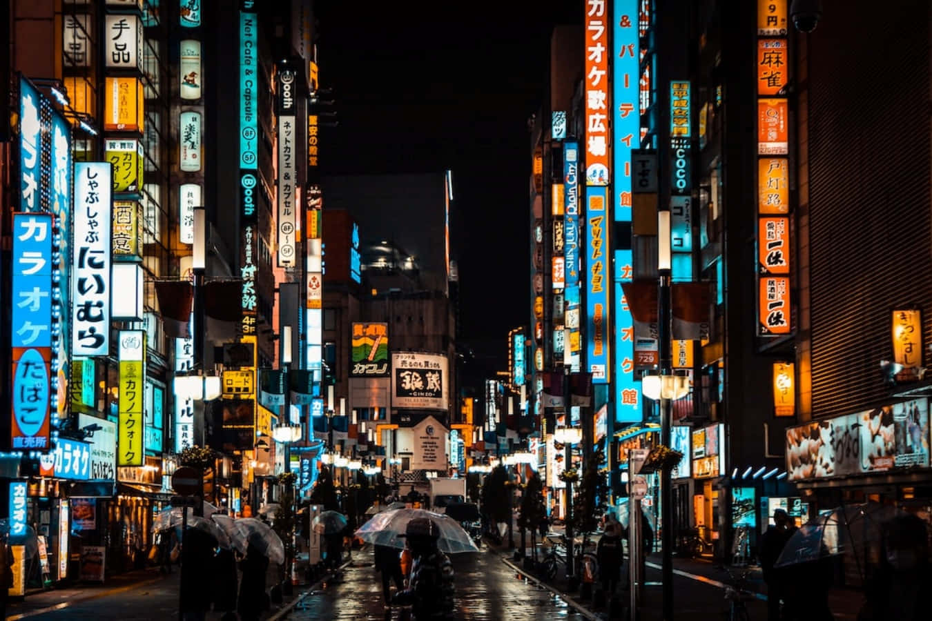 Street Light 桌布 壁紙 — 雨濕的東京小巷在夜晚閃爍著霓虹燈招牌，倒映在濕漉漉的人行道上，行人撐傘走過。