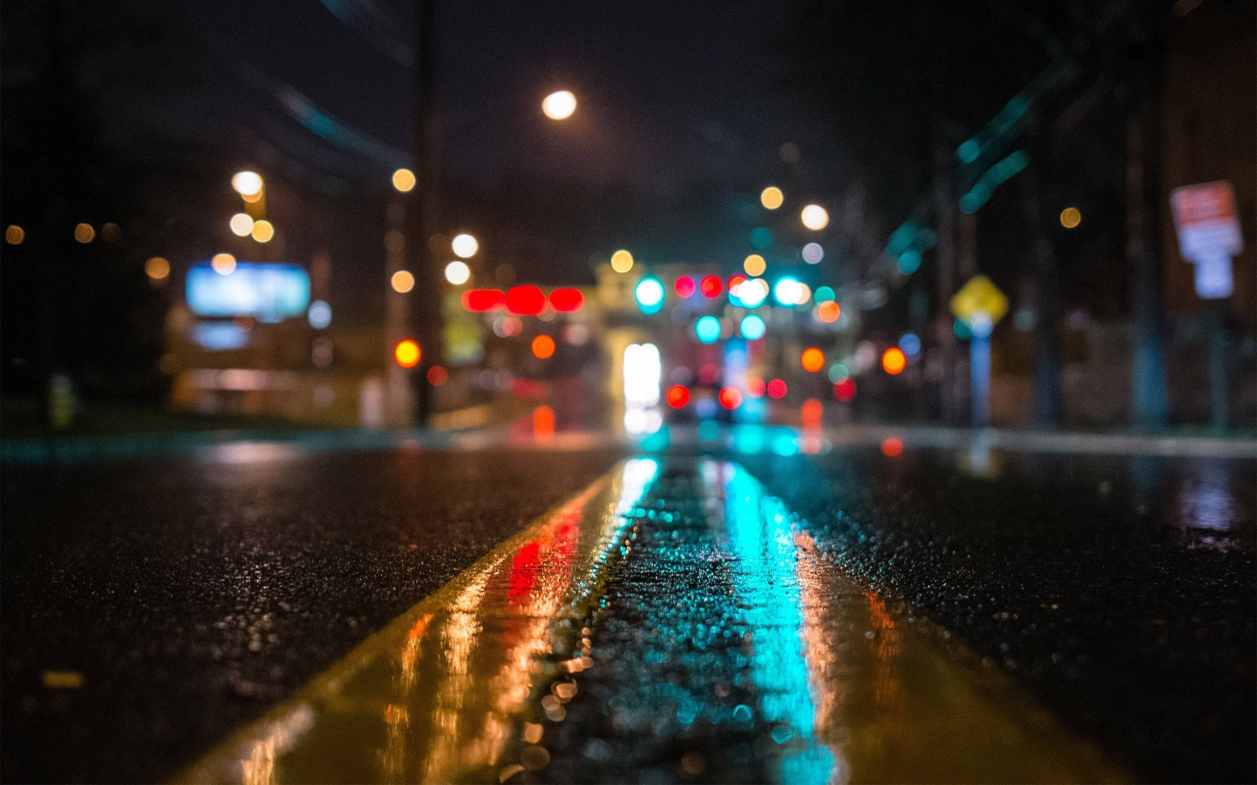 Mac 桌布 壁紙 — 雨濕的都市街道夜晚，發光的散景燈光反射在濕瀝青和黃色車道線上。