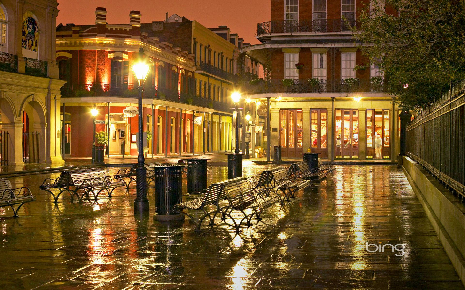french 桌布 壁紙 — 雨濕的鵝卵石街道在夜晚反射出歷史建築和發光商店櫥窗的溫暖金色燈光。