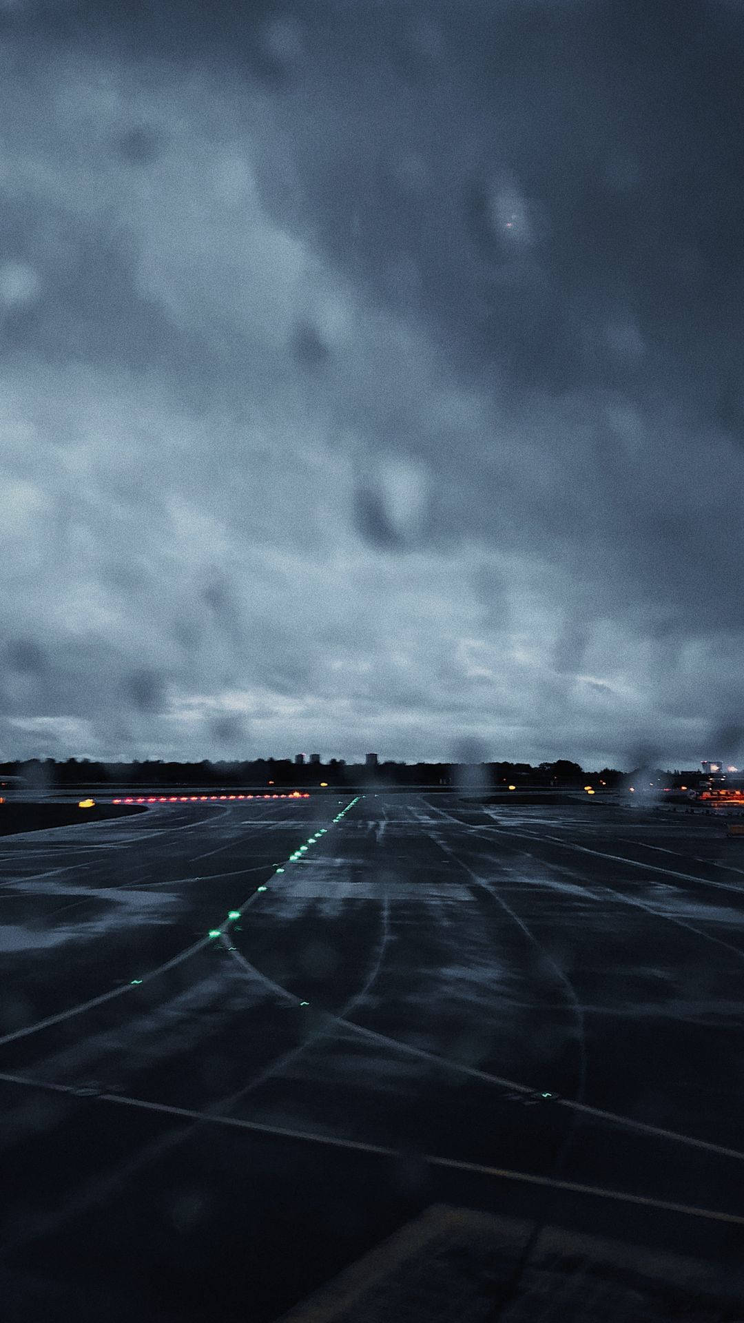 Runway 桌布 壁紙 — 雨痕模糊了黑暗的機場停機坪，在暴風雨的天空下，跑道燈閃爍發光。