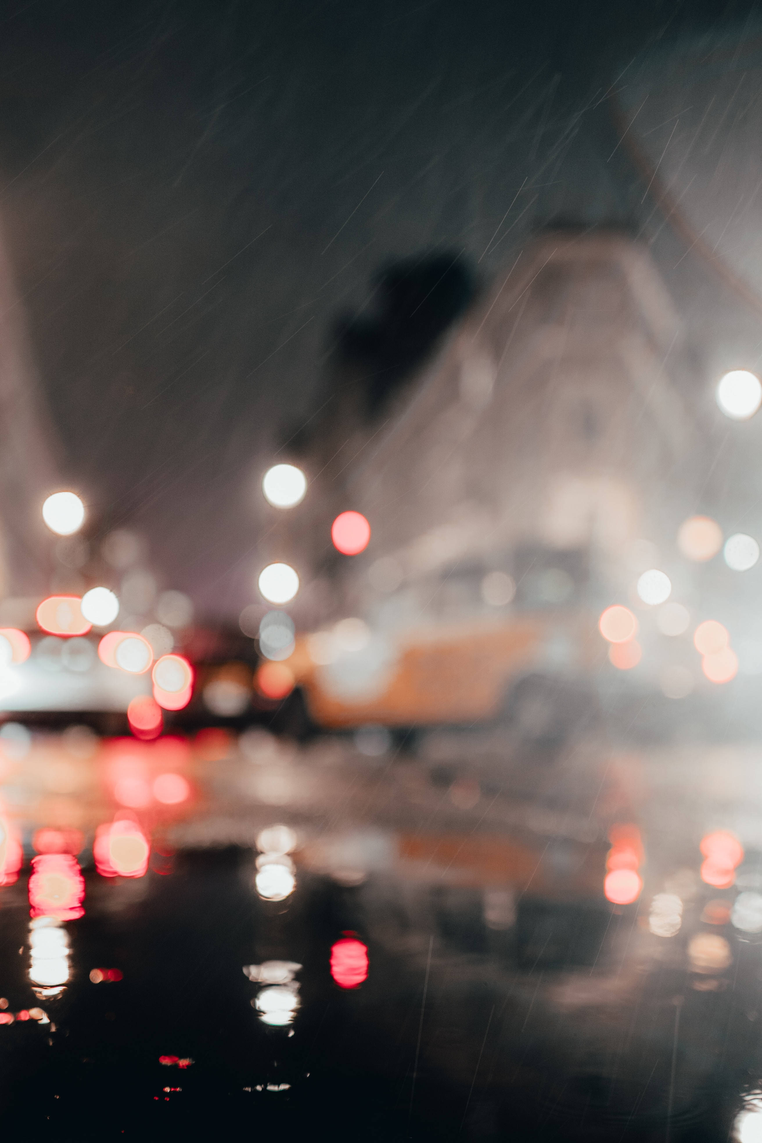 Bokeh 桌布 壁紙 — 雨絲將城市燈光模糊成發光球體，夜晚在濕漉漉的人行道上反射。