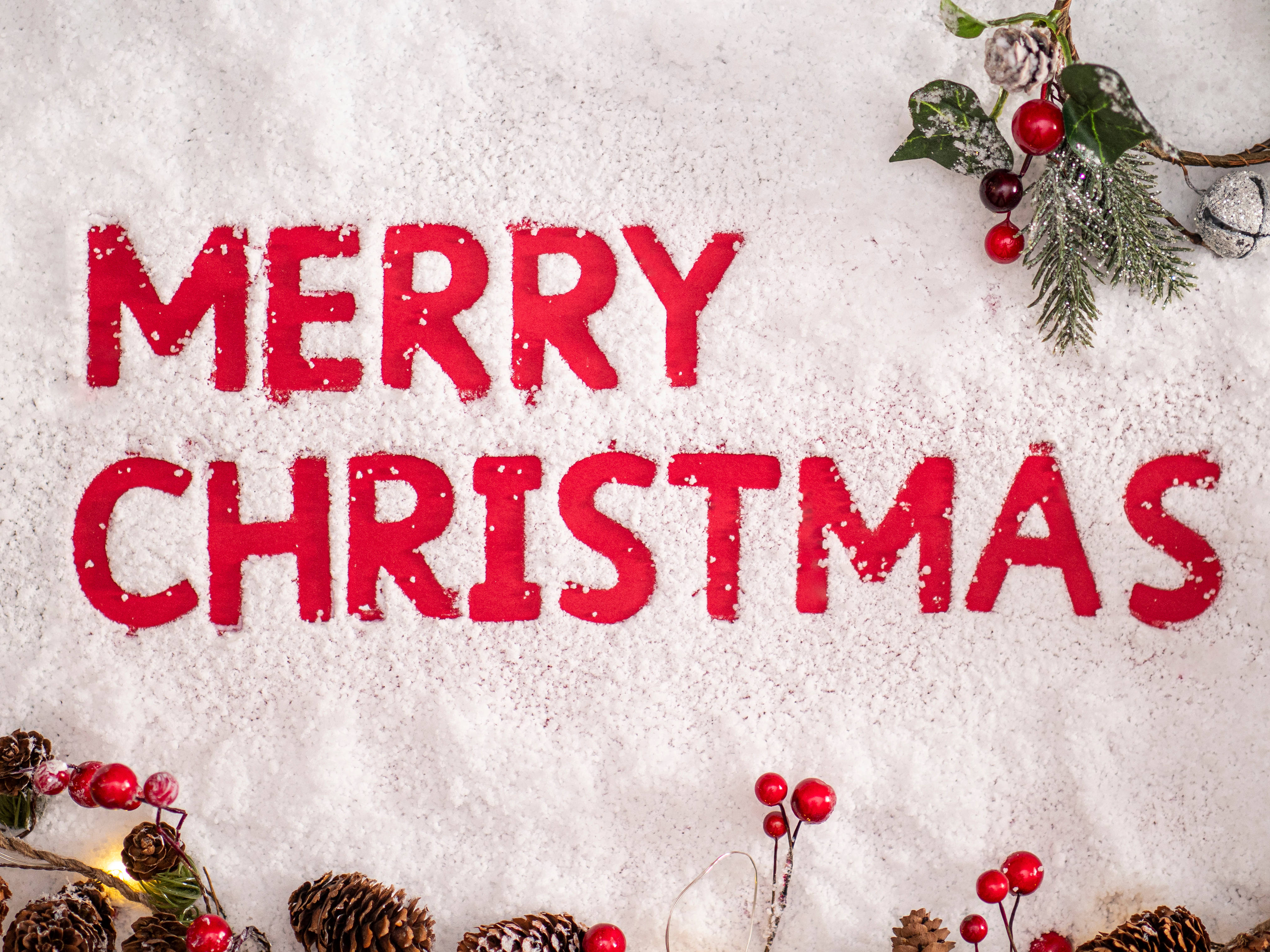聖誕快樂 桌布 壁紙 — 雪中形成的粗體紅色「MERRY CHRISTMAS」字母，並以節日松樹枝和紅莓裝飾角落。