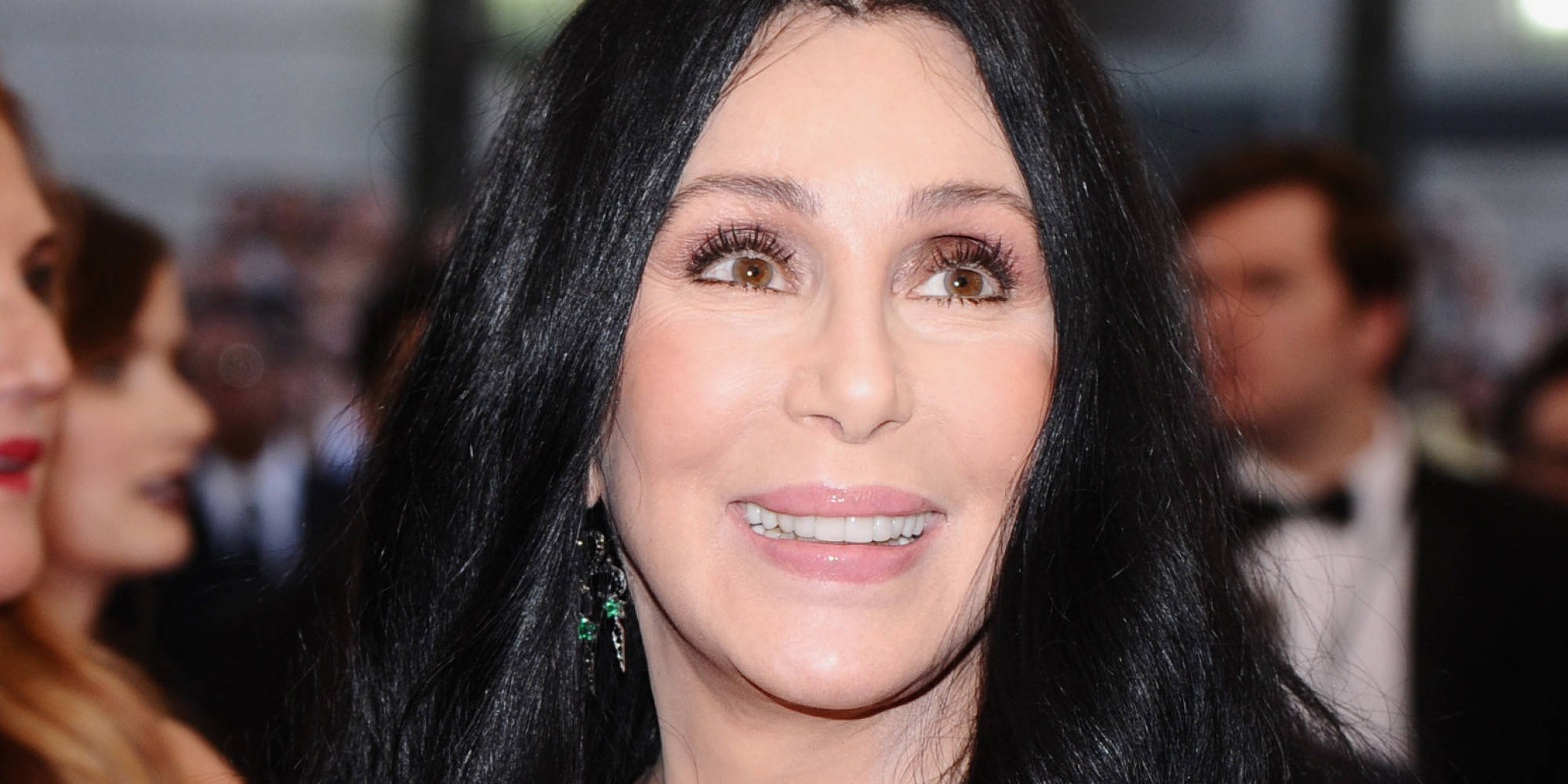 Celebrity 桌布 壁紙 — 雪兒（Cher）在華麗活動中微笑的近距離肖像，長黑髮配綠色耳環。