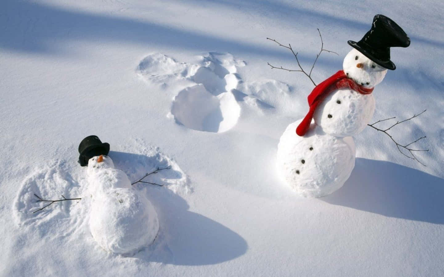 Winter 桌布 壁紙 — 雪地裡有兩個雪人，一個戴著高帽和圍巾站立，另一個躺著，兩者在明亮陽光下投下清晰陰影。
