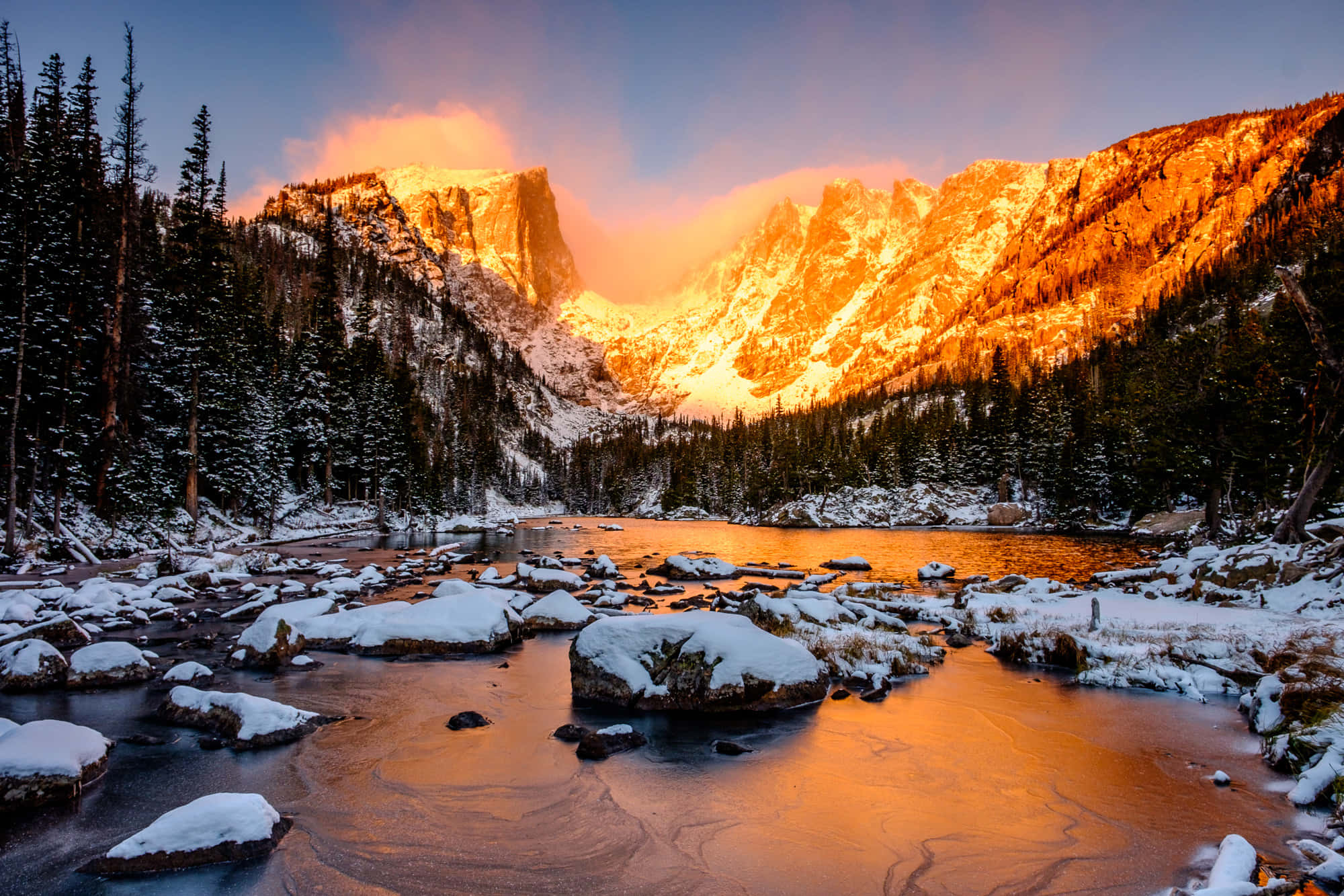 Colorado 桌布 壁紙 — 雪山在日落時閃耀琥珀色光芒，山峰倒映在被常青樹環繞的平靜河流中。