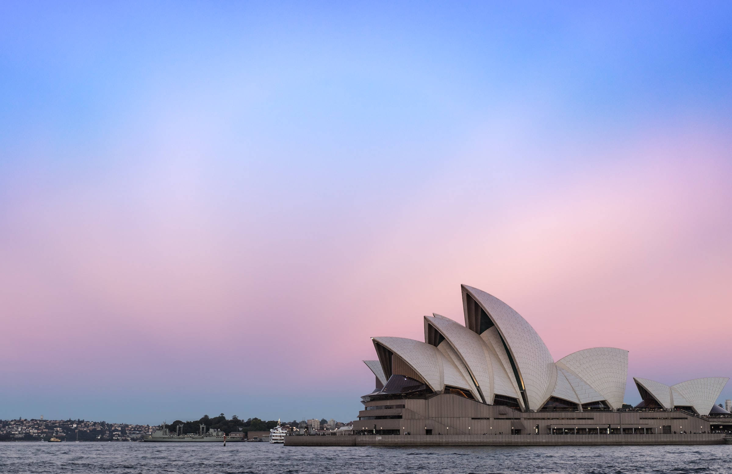 Sydney 桌布 壁紙 — 雪梨歌劇院的帆船造型，映襯著柔和粉紅與藍色的暮色天空，下方是平靜的港灣水面。