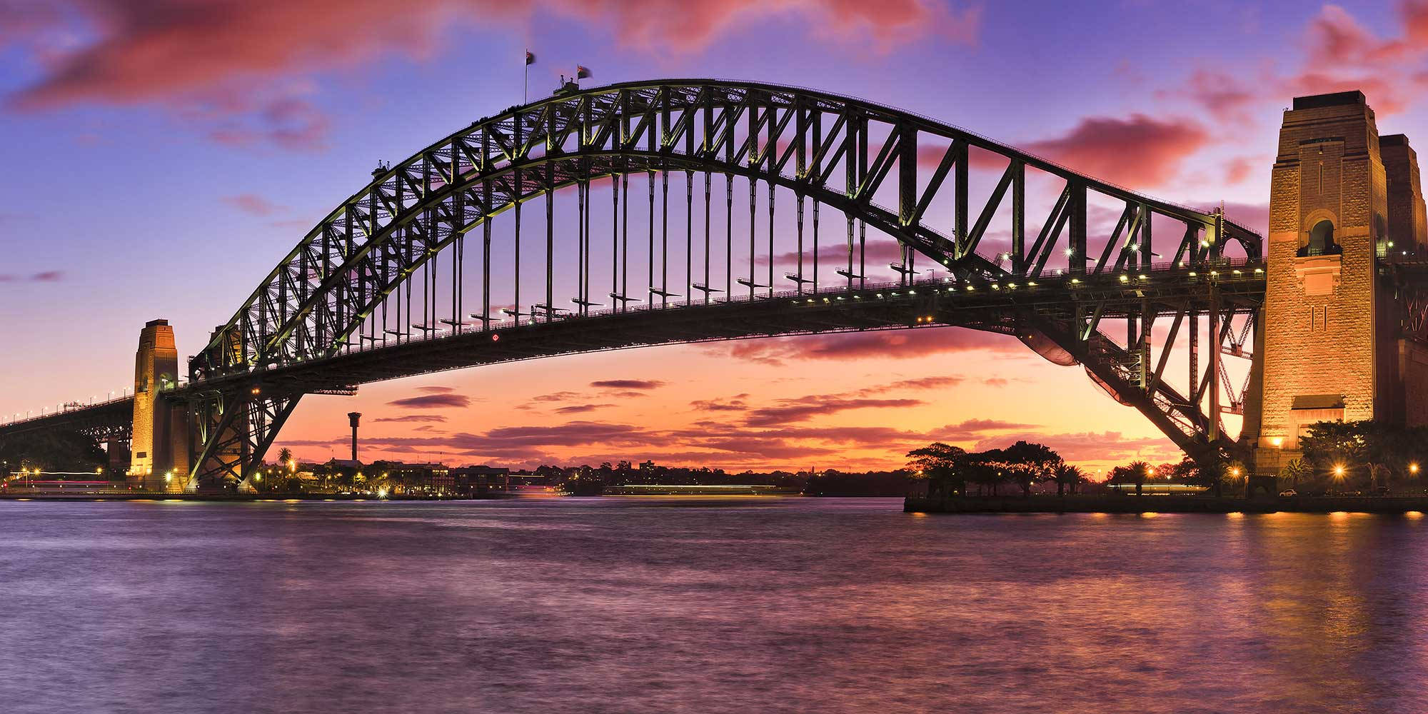 Sydney 桌布 壁紙 — 雪梨港灣大橋在熾熱的夕陽天空下閃耀，倒映在下方平靜的水面上。