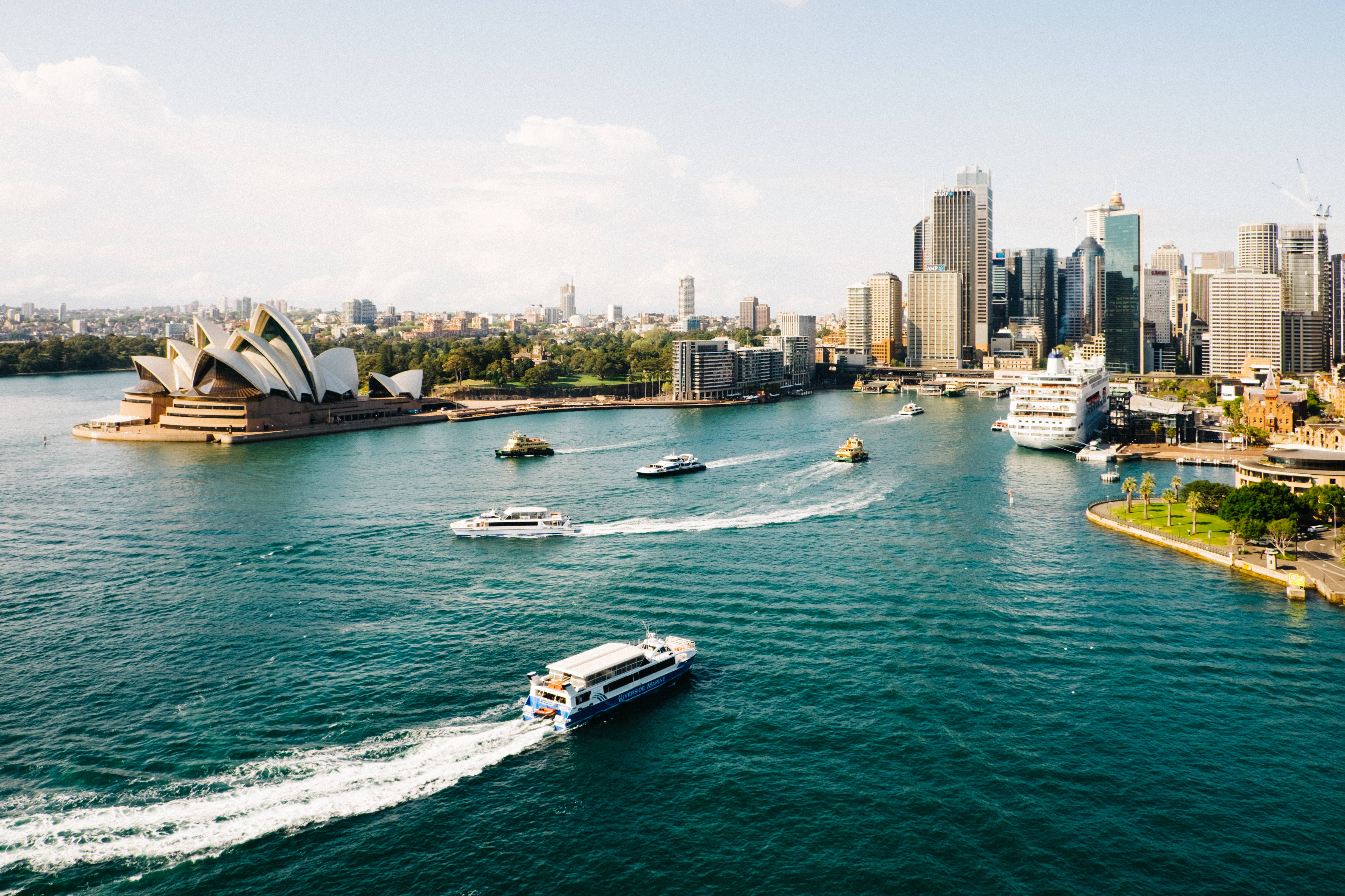Sydney 桌布 壁紙 — 雪梨港的鳥瞰圖，標誌性的歌劇院和現代摩天大樓，船隻在碧綠的水面上滑行。
