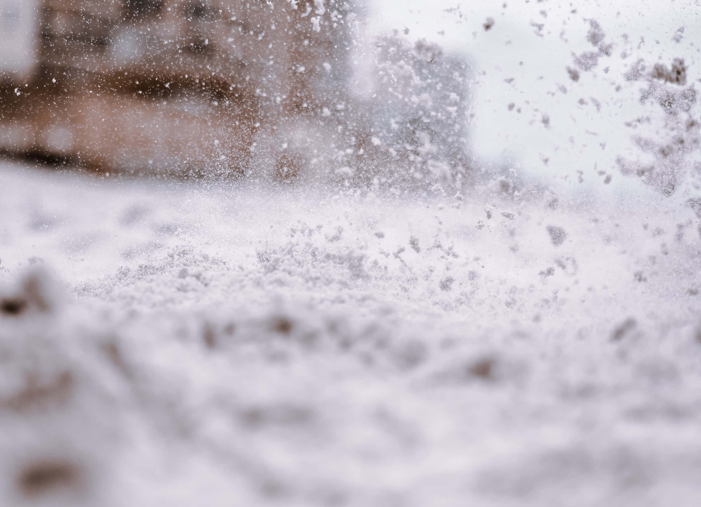 Snowing 桌布 壁紙 — 雪花在半空中懸浮的特寫，背景是模糊的城市景觀，帶有柔和的白色和灰色色調。