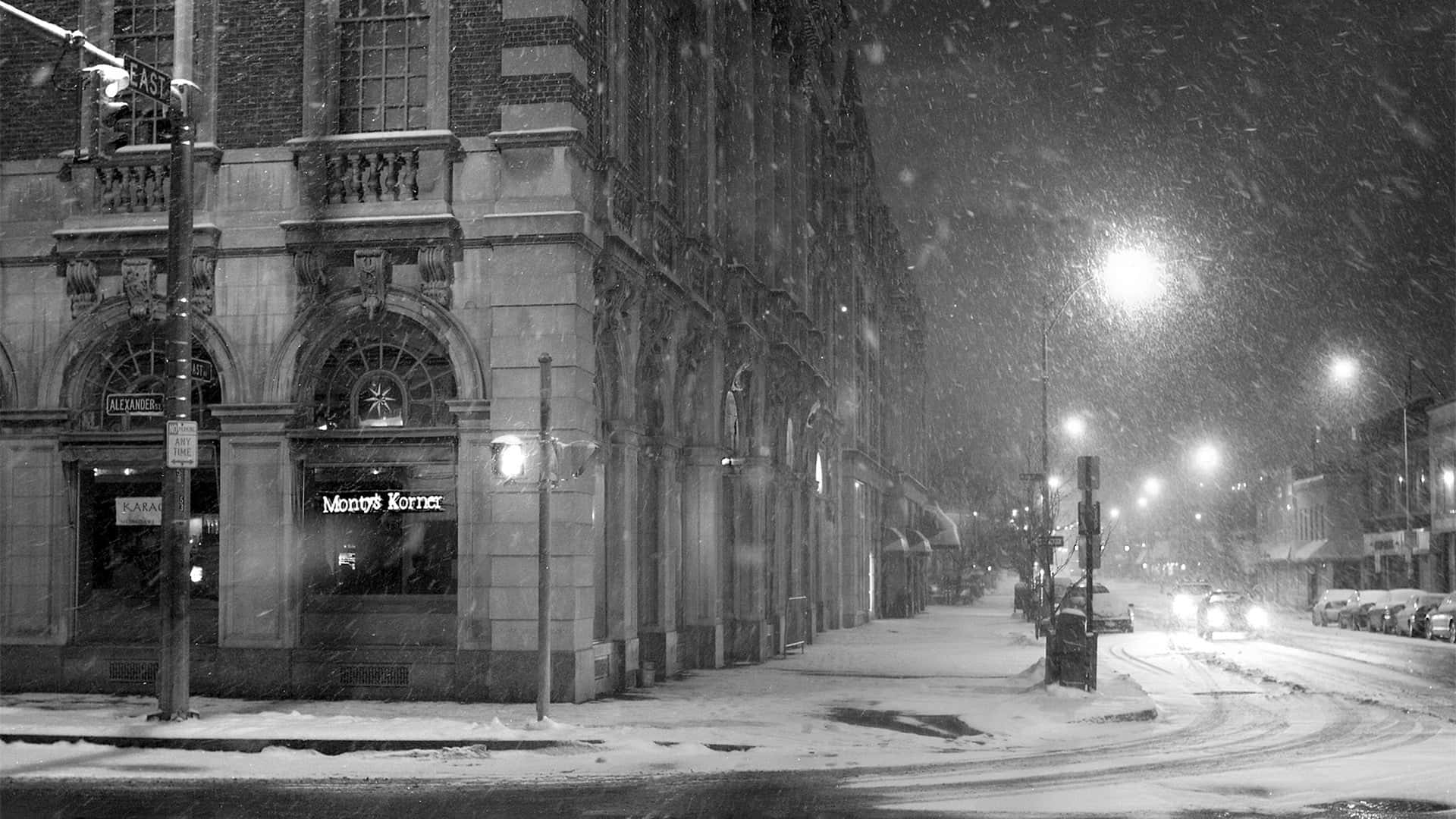 Black And White City 桌布 壁紙 — 雪花在單色城市夜景中旋轉，街燈照亮了積雪的人行道和停泊的汽車。