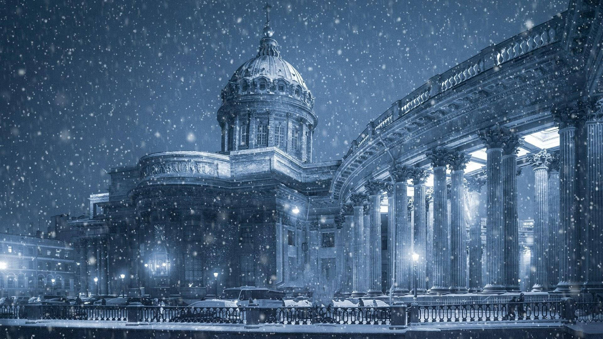 Saint Petersburg 桌布 壁紙 — 雪花在夜空中飄蕩，飄過一座宏偉的新古典主義建築，建築物有發光的燈光和積雪的柱子。