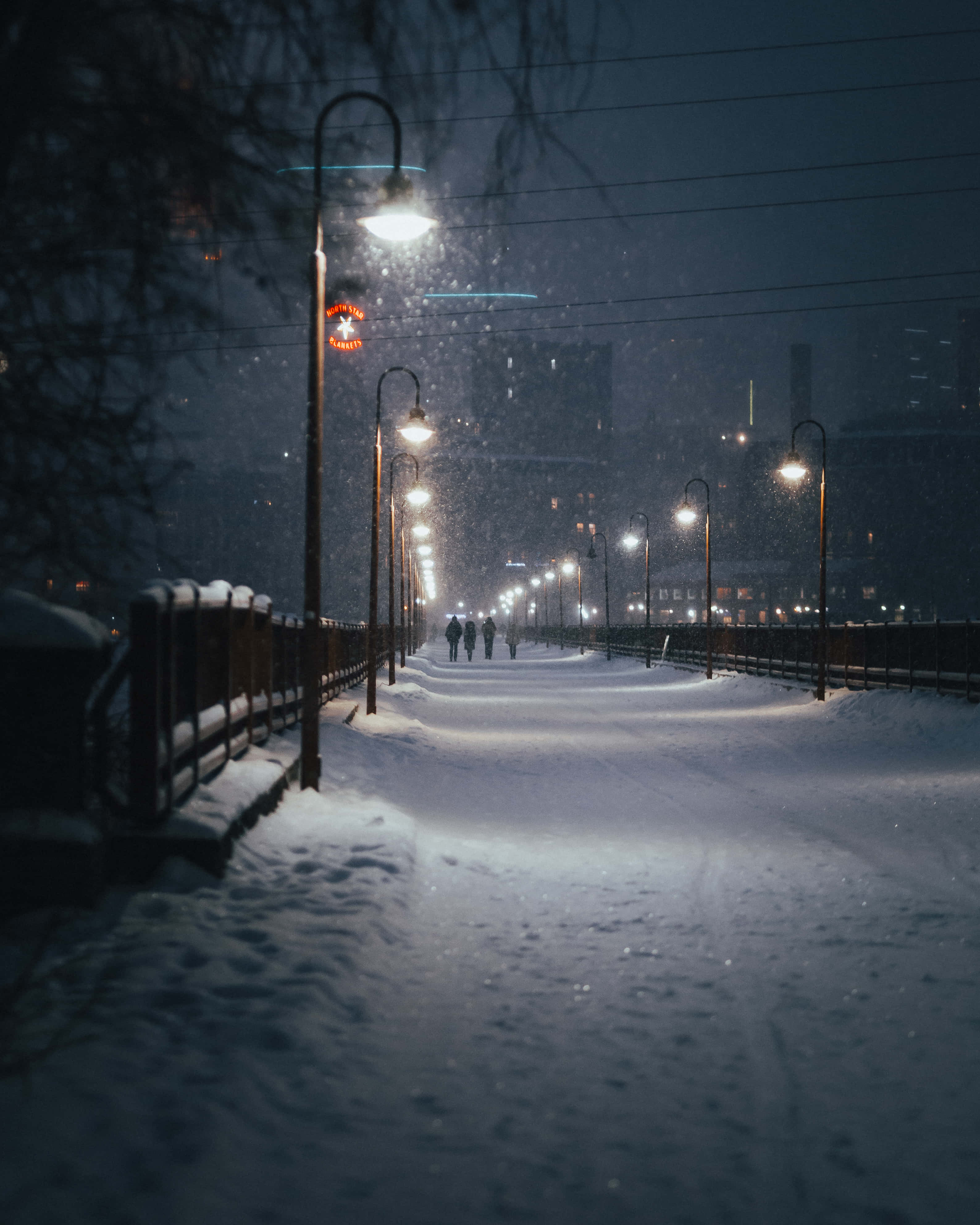 冬天 桌布 壁紙 — 雪花在夜間沿著安靜的積雪城市步道，在發光的街燈下飄舞。