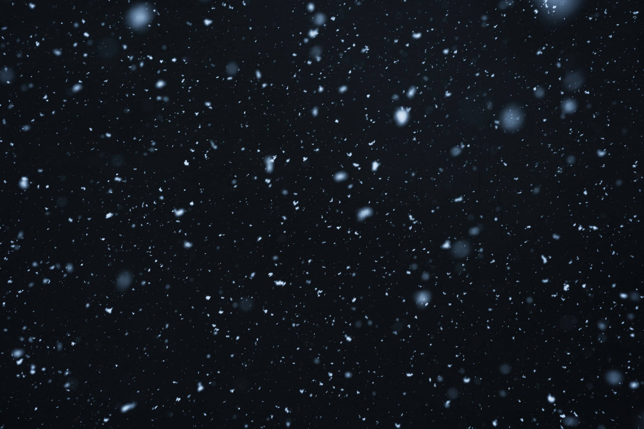 黑色 桌布 壁紙 — 雪花在深邃的黑色背景上輕輕飄落，營造出寧靜的冬日場景。