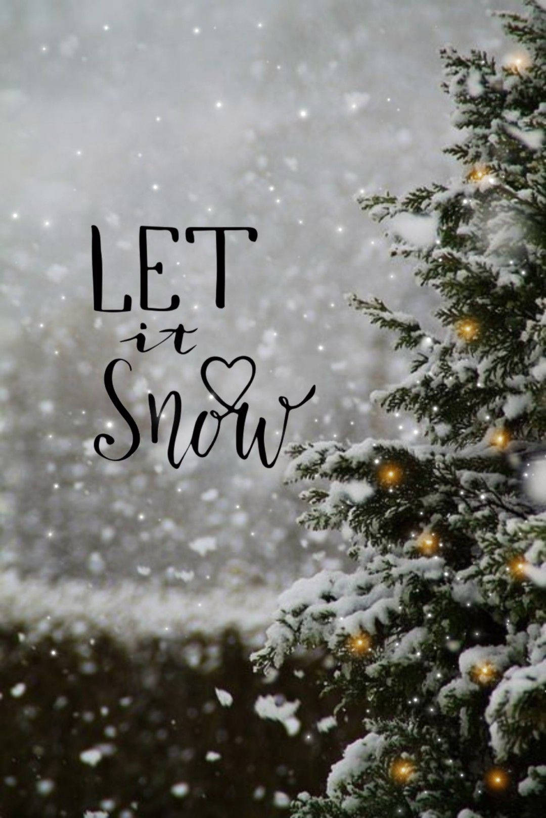 Snowy Christmas 桌布 壁紙 — 雪花輕輕飄落在被雪覆蓋的松樹周圍，樹上裝飾著溫暖的燈光和優雅字體的「let it snow」字樣。