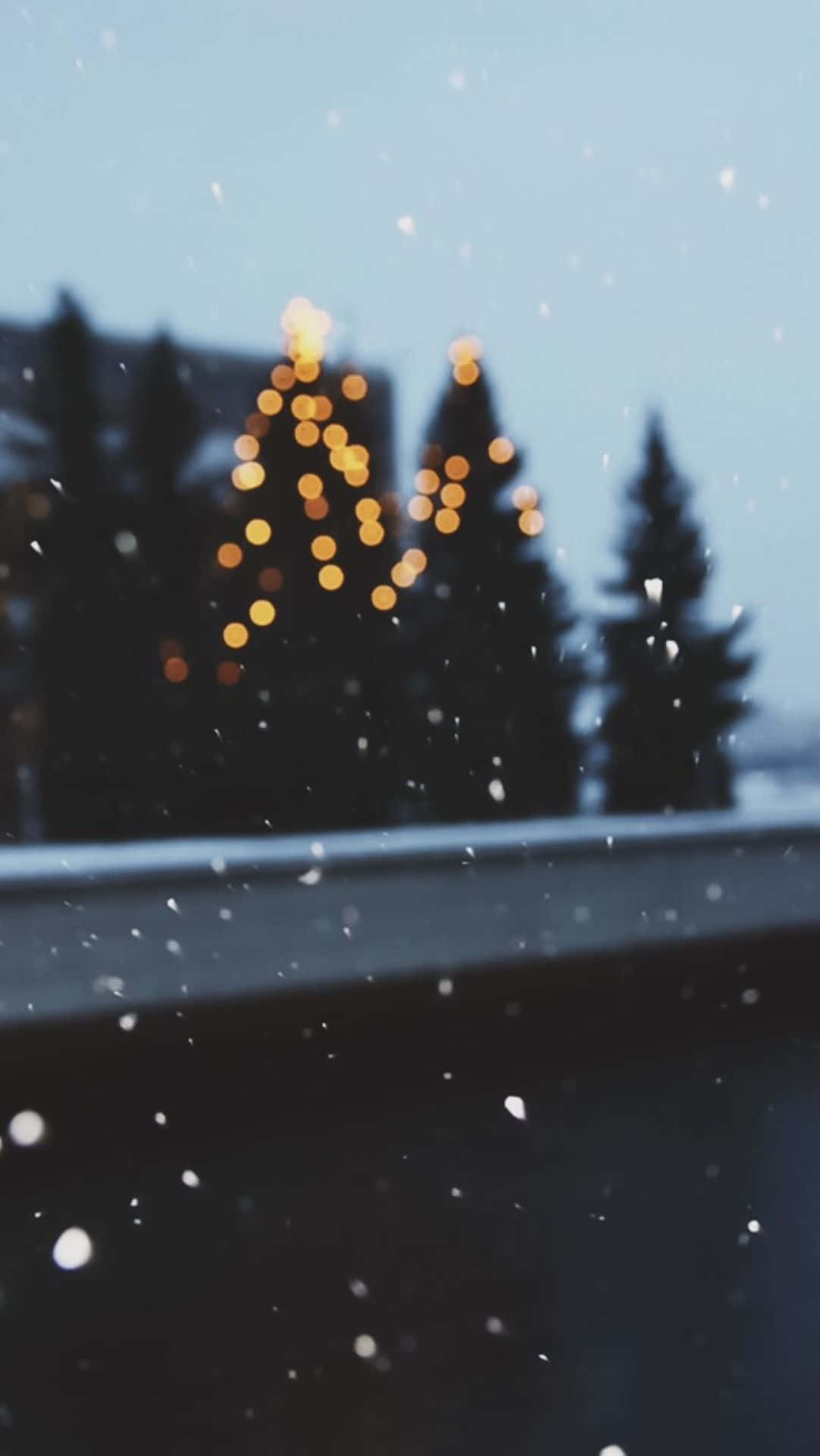 聖誕美學 桌布 壁紙 — 雪花飄過車窗，模糊的金色燈光在暮色天空中形成聖誕樹的剪影。