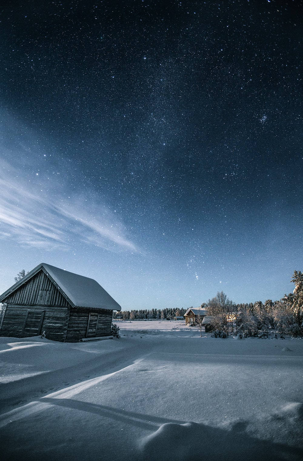 Winter House 桌布 壁紙 — 雪覆蓋的木屋，在繁星點點的冬夜天空下，上方有微弱的極光絲縷。