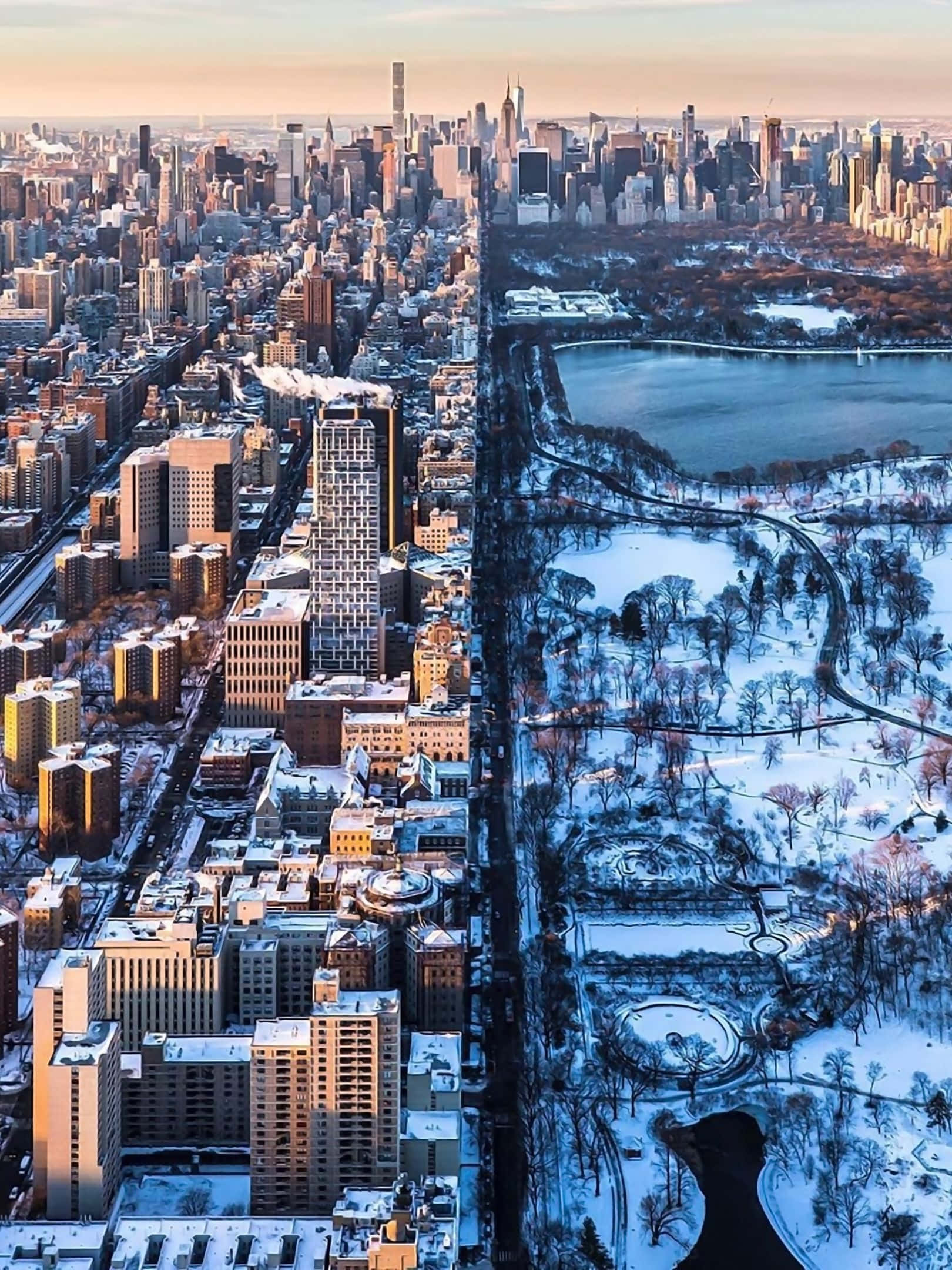 1620x2160 桌布 壁紙 — 雪覆蓋的紐約市鳥瞰圖，中央公園的冰凍湖泊和光禿樹木與黃金時段的城市天際線形成對比。