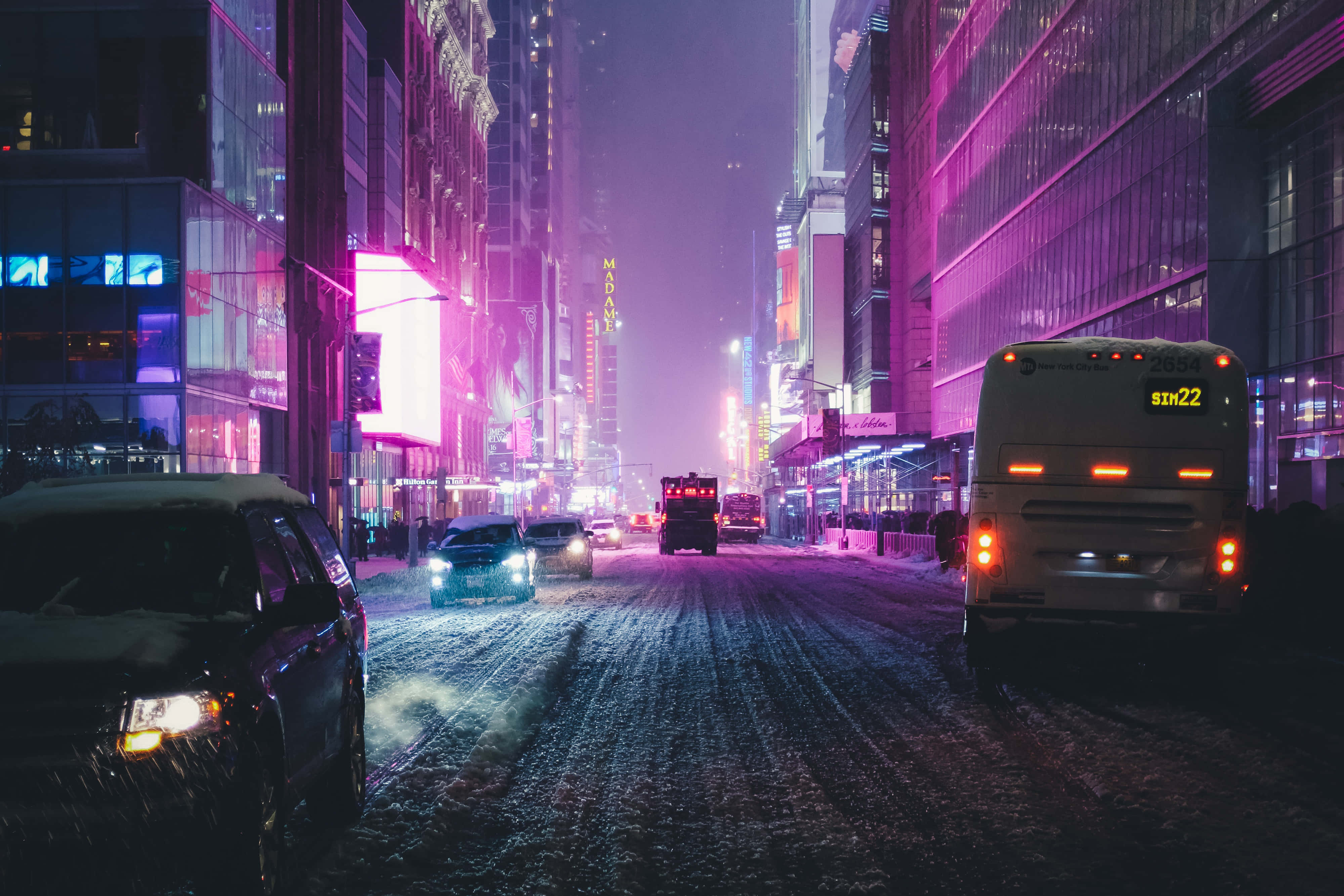 夜景城市 桌布 壁紙 — 雪覆蓋著一條被霓虹燈浸透的夜間城市街道，汽車和巴士在發光的城市峽谷中滑行。