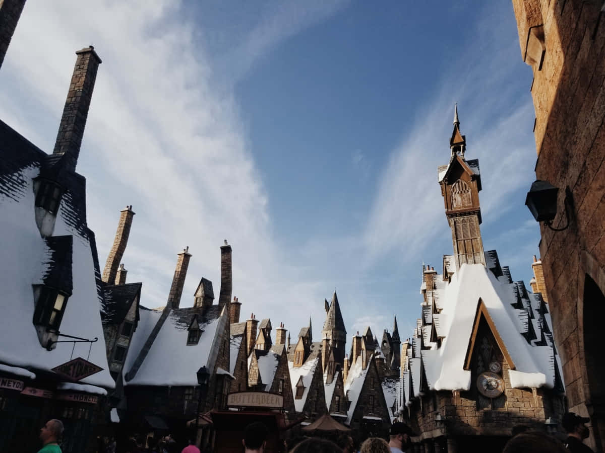 Hogsmeade 桌布 壁紙 — 雪覆蓋著斜角巷巫師建築物陡峭的屋頂，天空湛藍，雲朵輕柔。