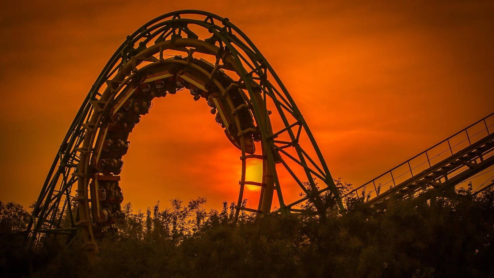 Roller Coaster 桌布 壁紙 — 雲霄飛車在火紅橙色日落天空的襯托下形成剪影，前景有樹木。
