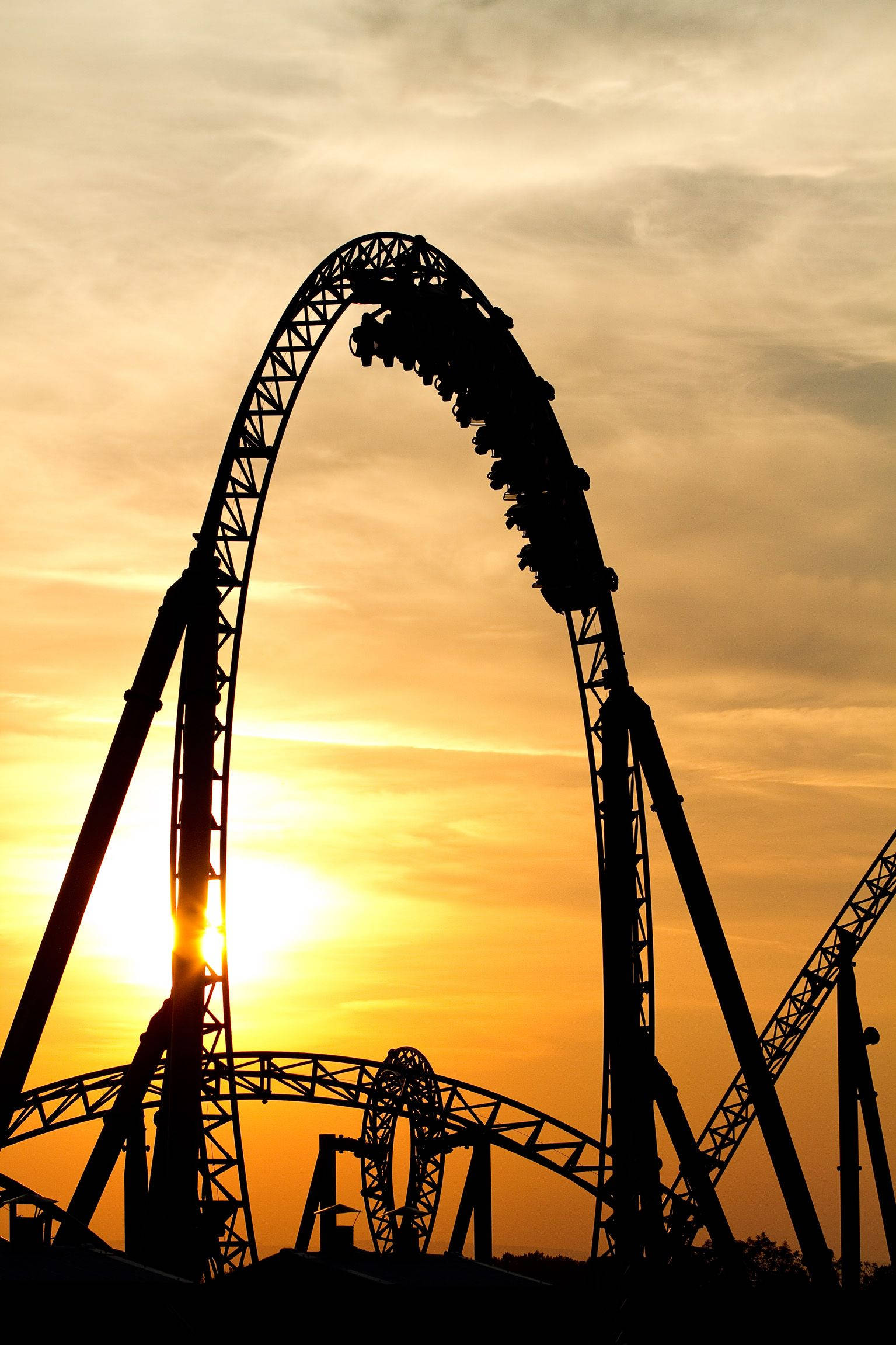 Roller Coaster 桌布 壁紙 — 雲霄飛車在金色日落天空的襯托下形成剪影，太陽從其拱門中窺視。