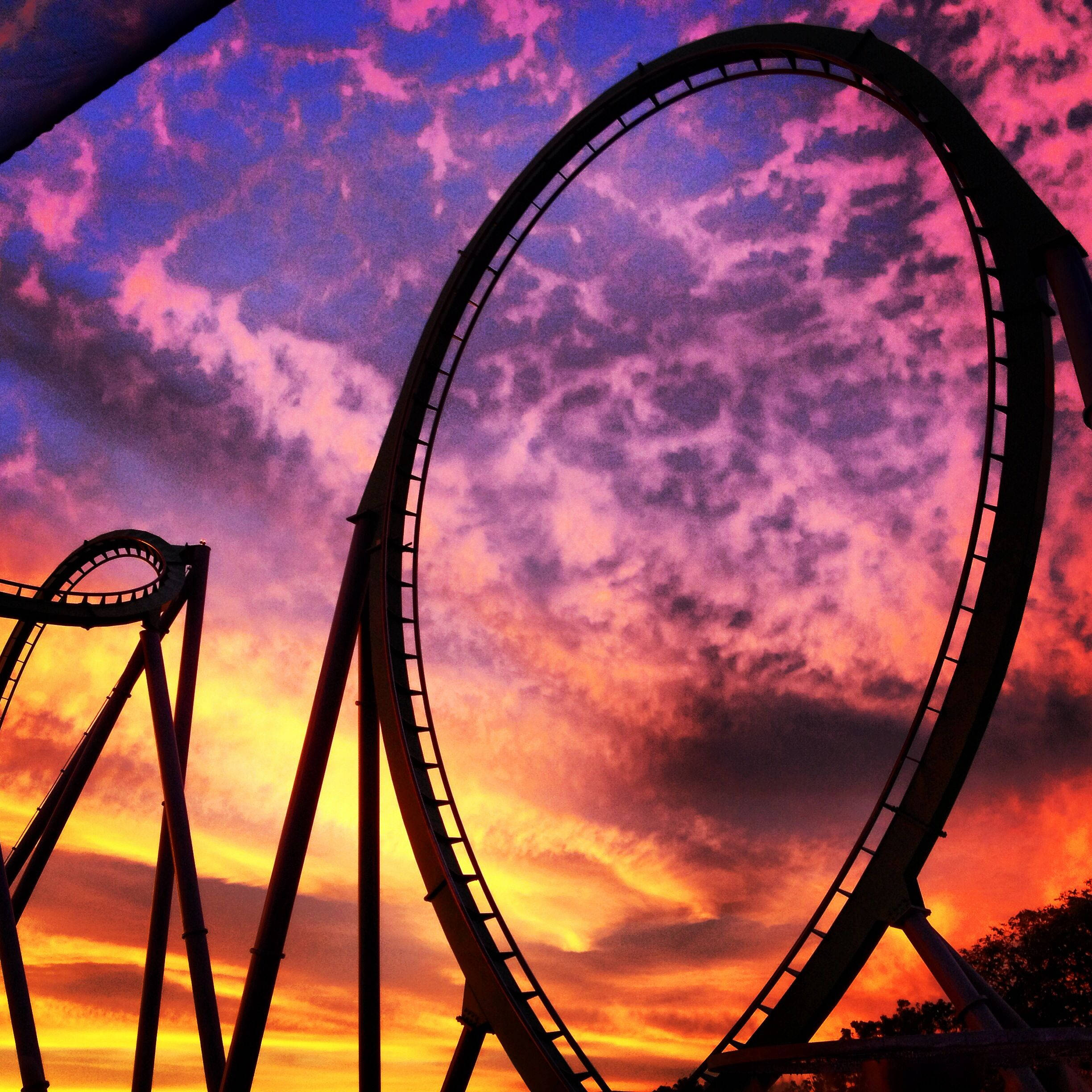 Roller Coaster 桌布 壁紙 — 雲霄飛車的剪影在紫、橙、藍色雲彩繪成的火紅夕陽天空下形成戲劇性的迴圈。