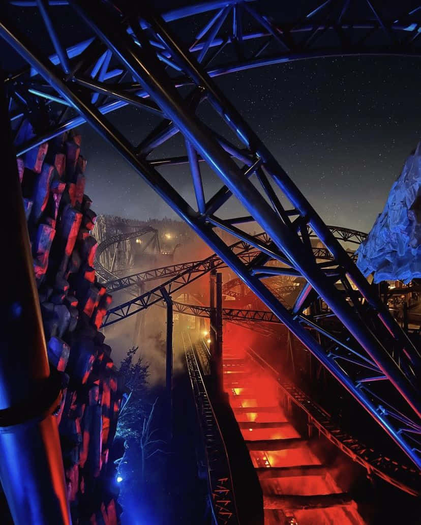 Six Flags 桌布 壁紙 — 雲霄飛車軌道在夜燈下發出紅藍光芒，映襯著星空，下方有薄霧繚繞。